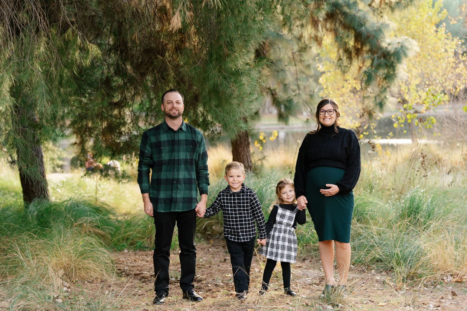 Family posing together in a natural outdoor setting with autumn trees and tall grass in the background.