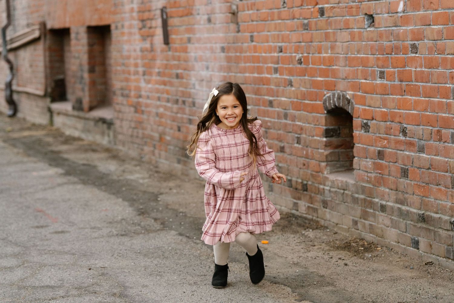 Child in pink dress running playfully along brick wall.