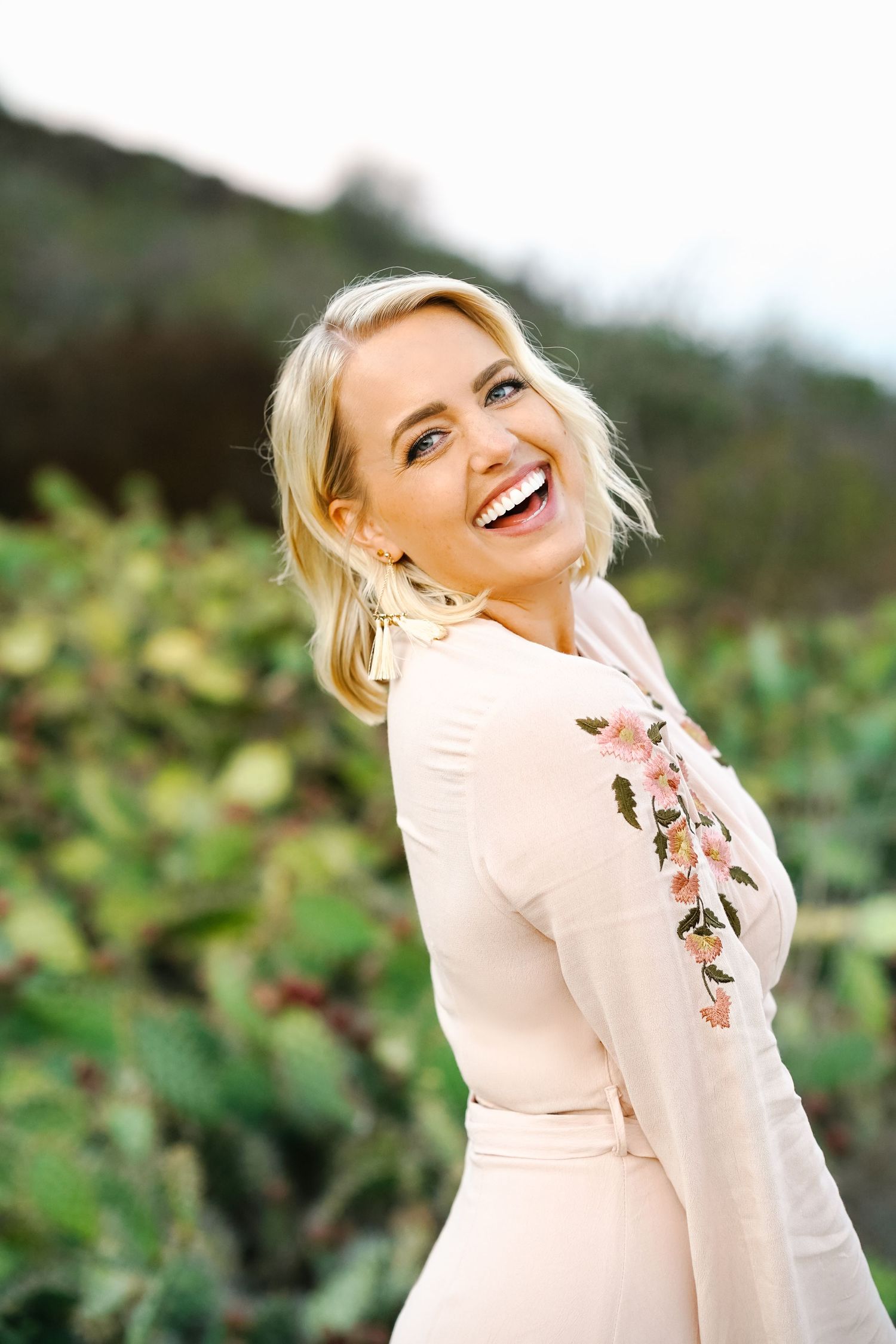 Woman in pink floral dress laughing joyfully outdoors with natural background.