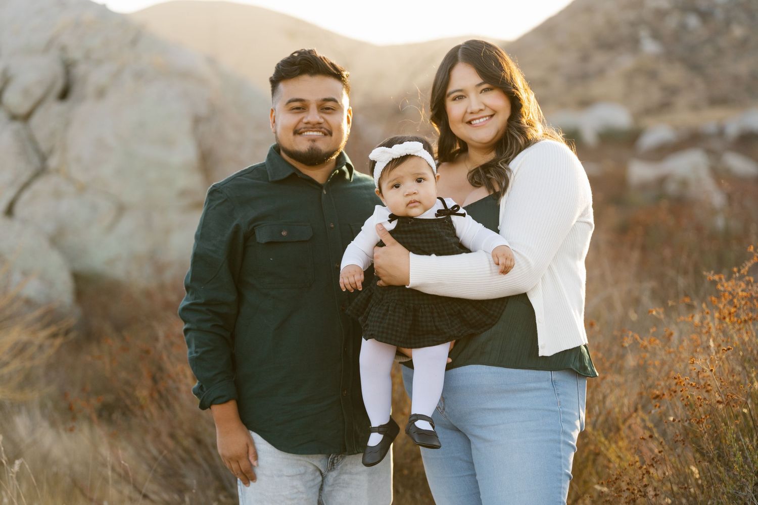Family dressed in casual attire poses against desert mountain backdrop at sunset.