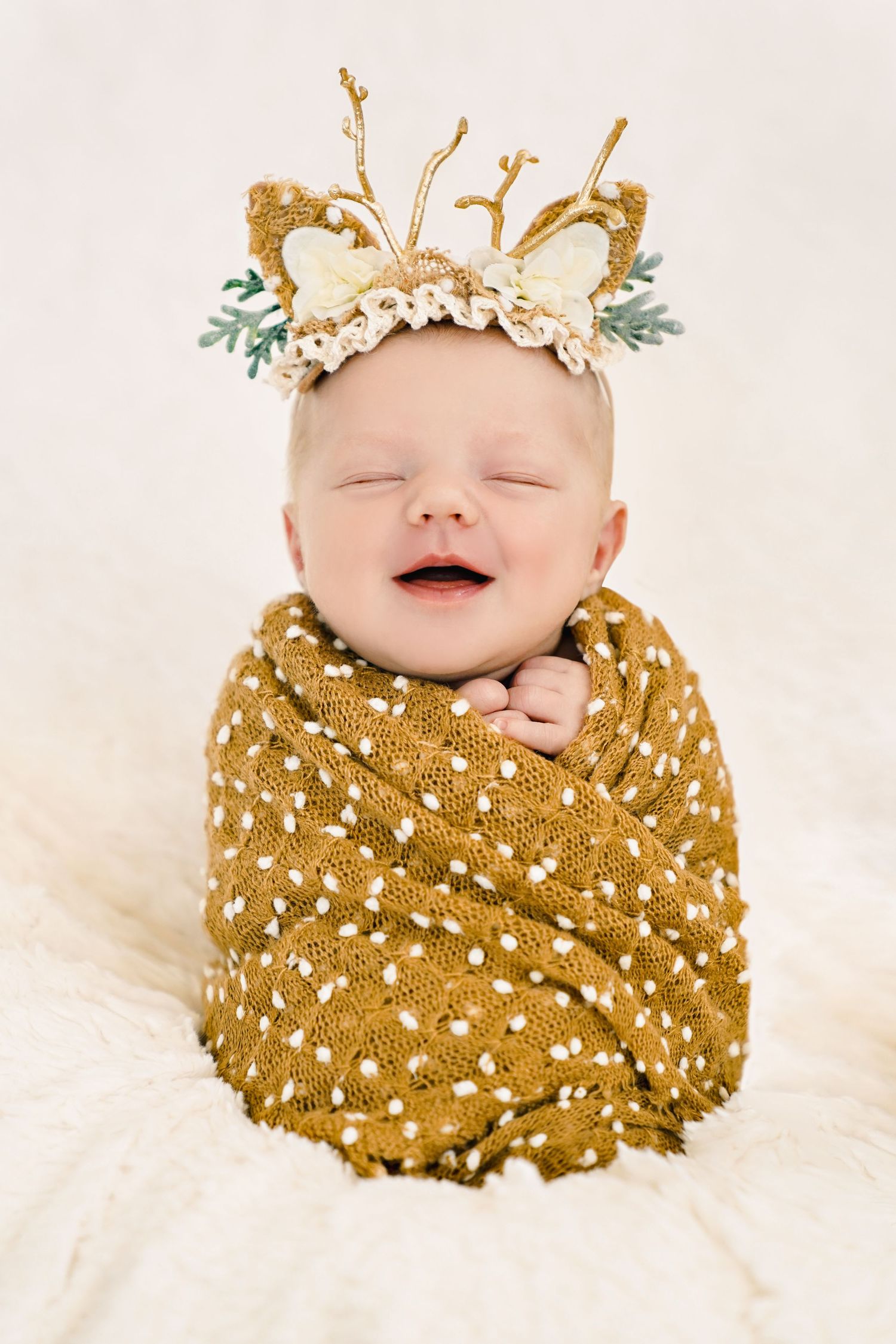 Baby wrapped in mustard polka dot blanket wearing decorative antler crown and flowers.