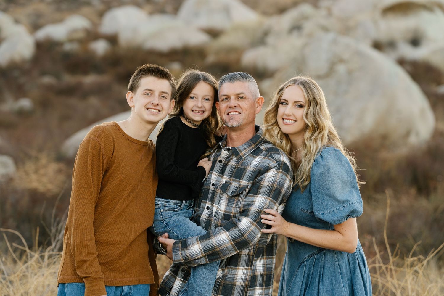 Family of four posing together against rocky desert landscape at sunset.