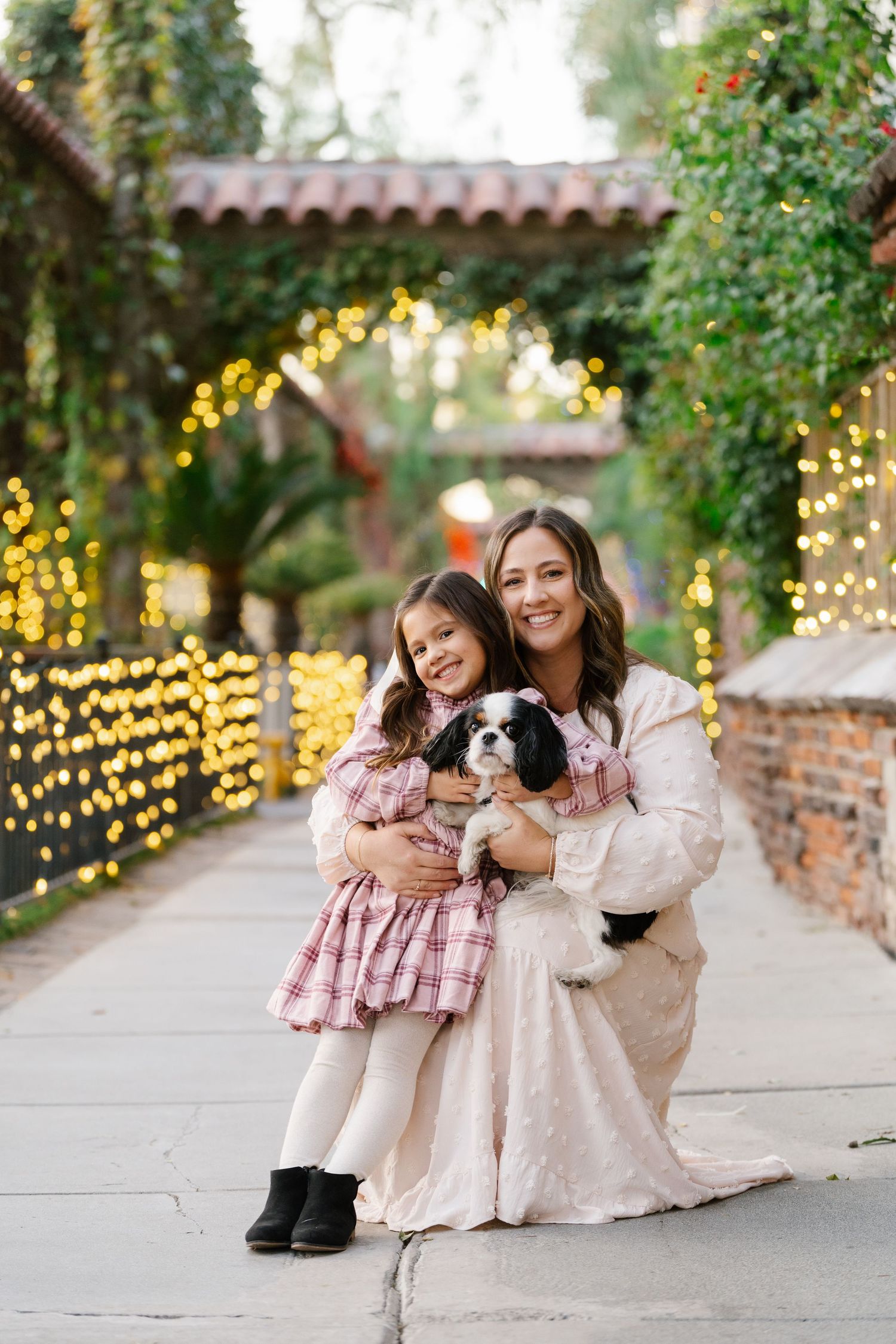 Family photoshoot with a small dog against a garden backdrop with twinkling lights.