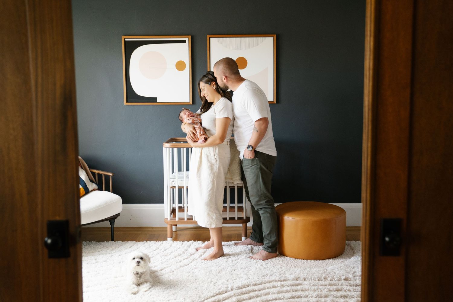 A family moment captured in a modern nursery with dark walls and white furniture.
