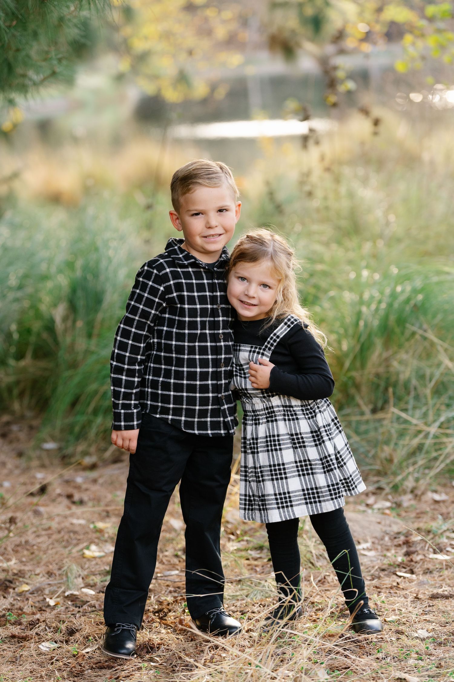 Siblings in matching plaid outfits pose together in an outdoor natural setting.