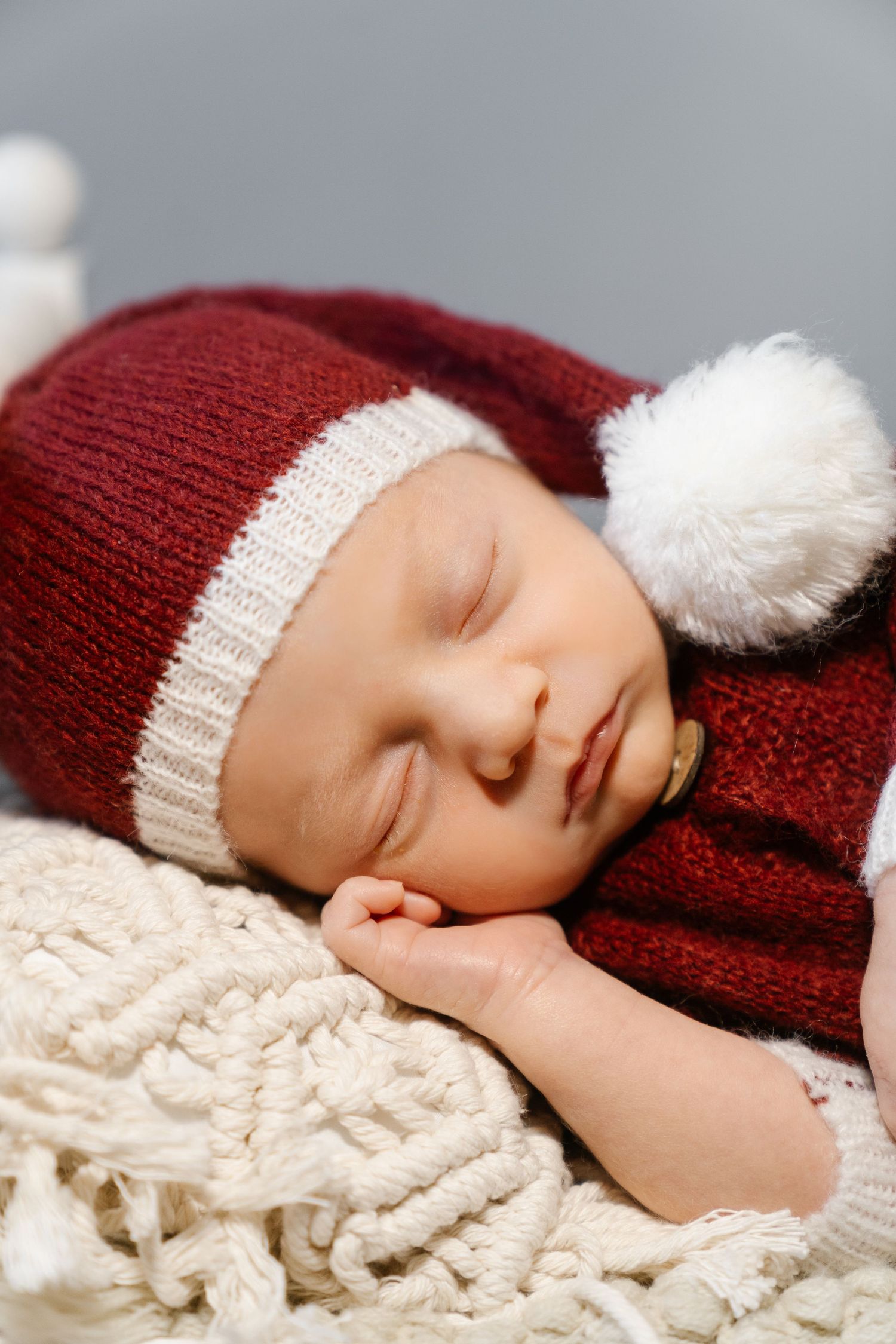 Sleeping baby wearing red and white knit santa hat on cream textured blanket.