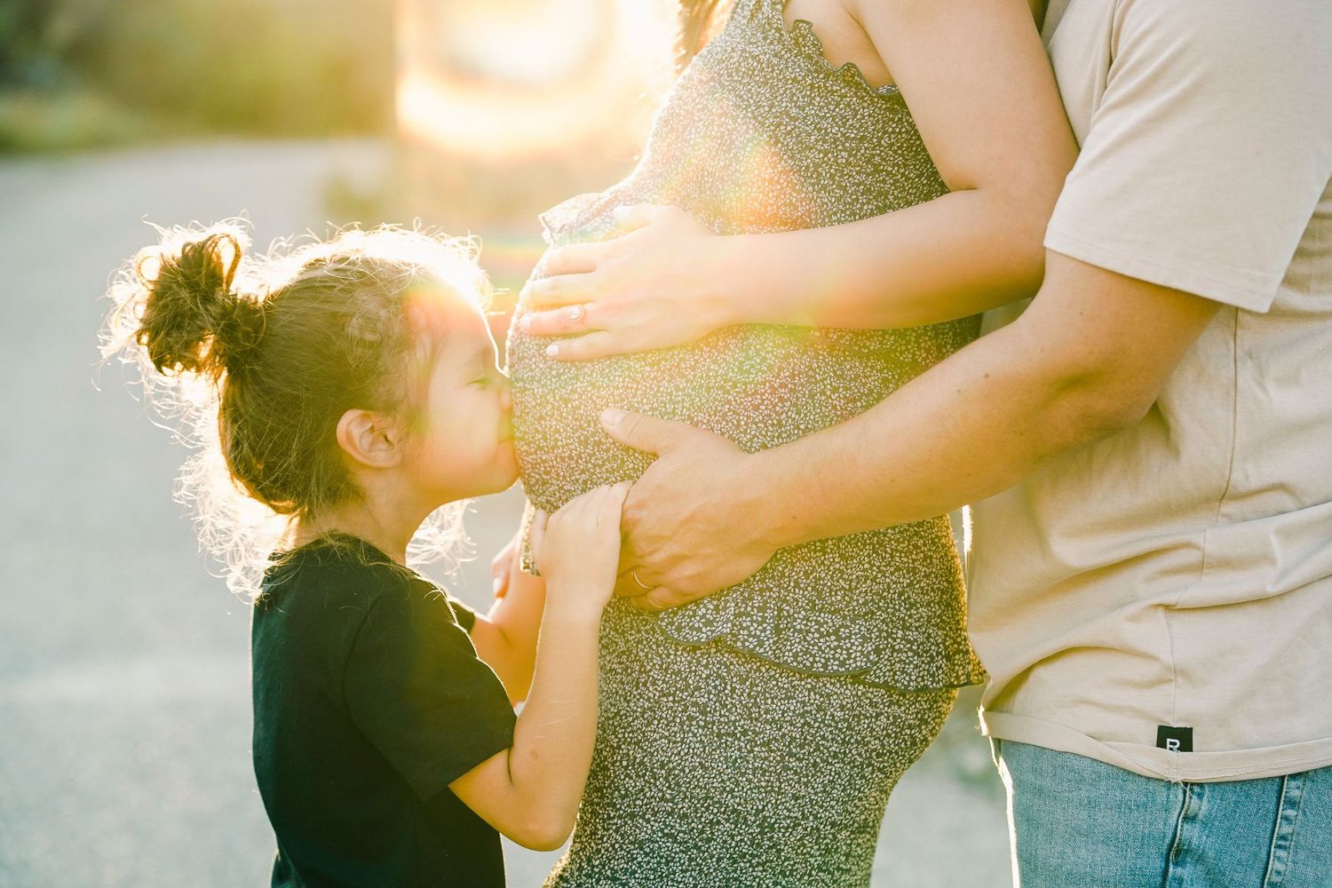 Family maternity moment captured in sunset light with child touching pregnant belly.