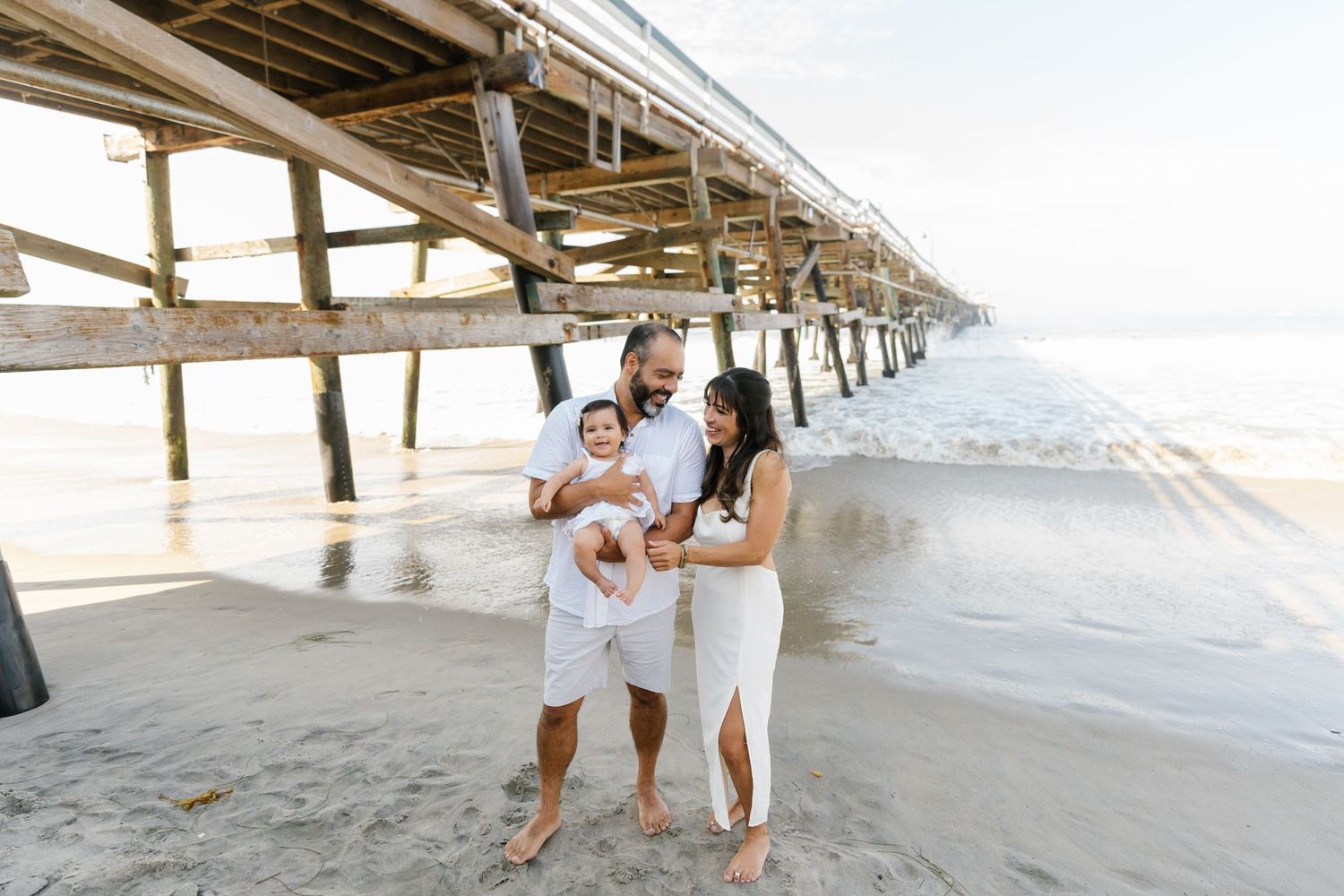Family sharing candid moment under wooden pier at beach.