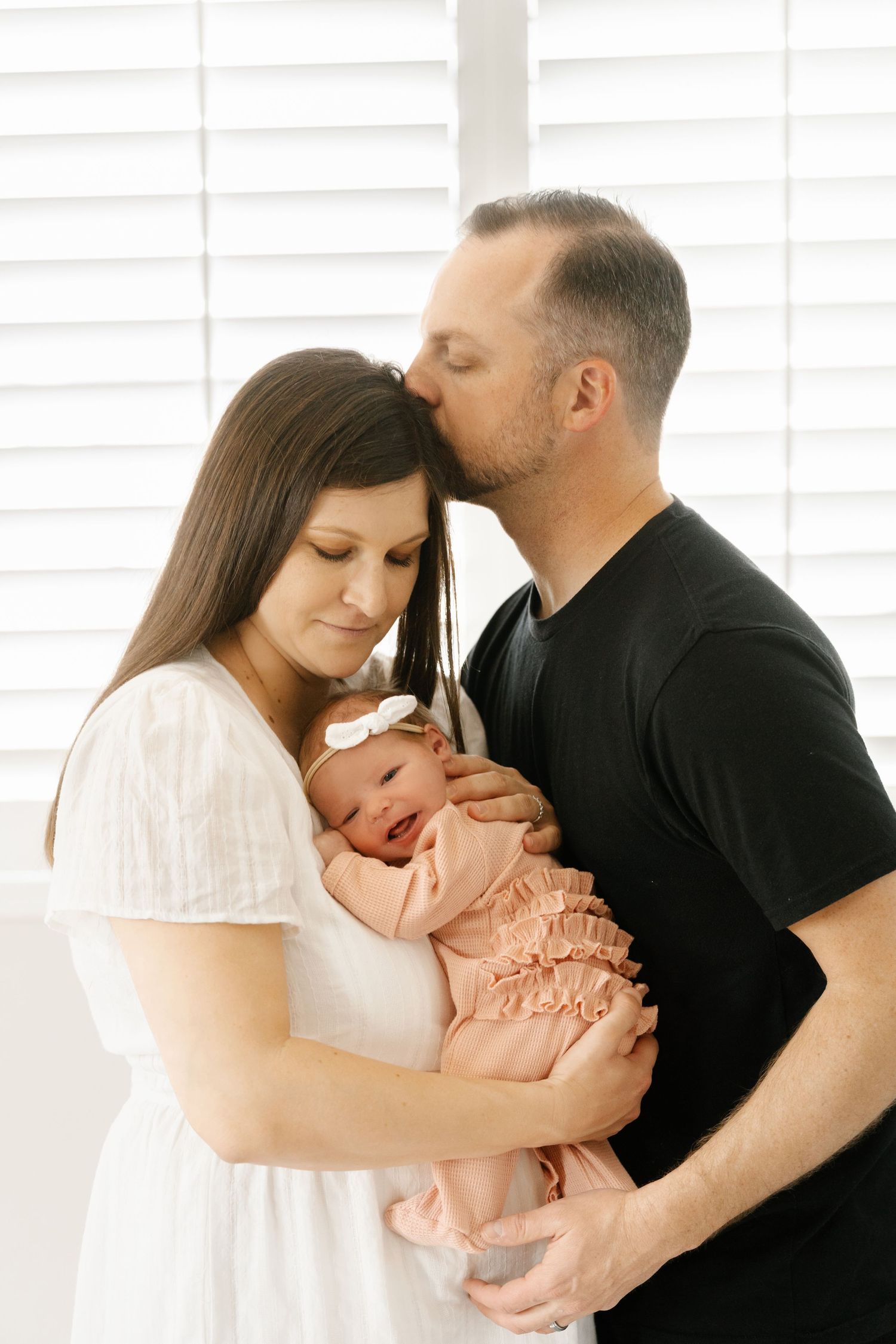 Family portrait in soft lighting against white shutters.