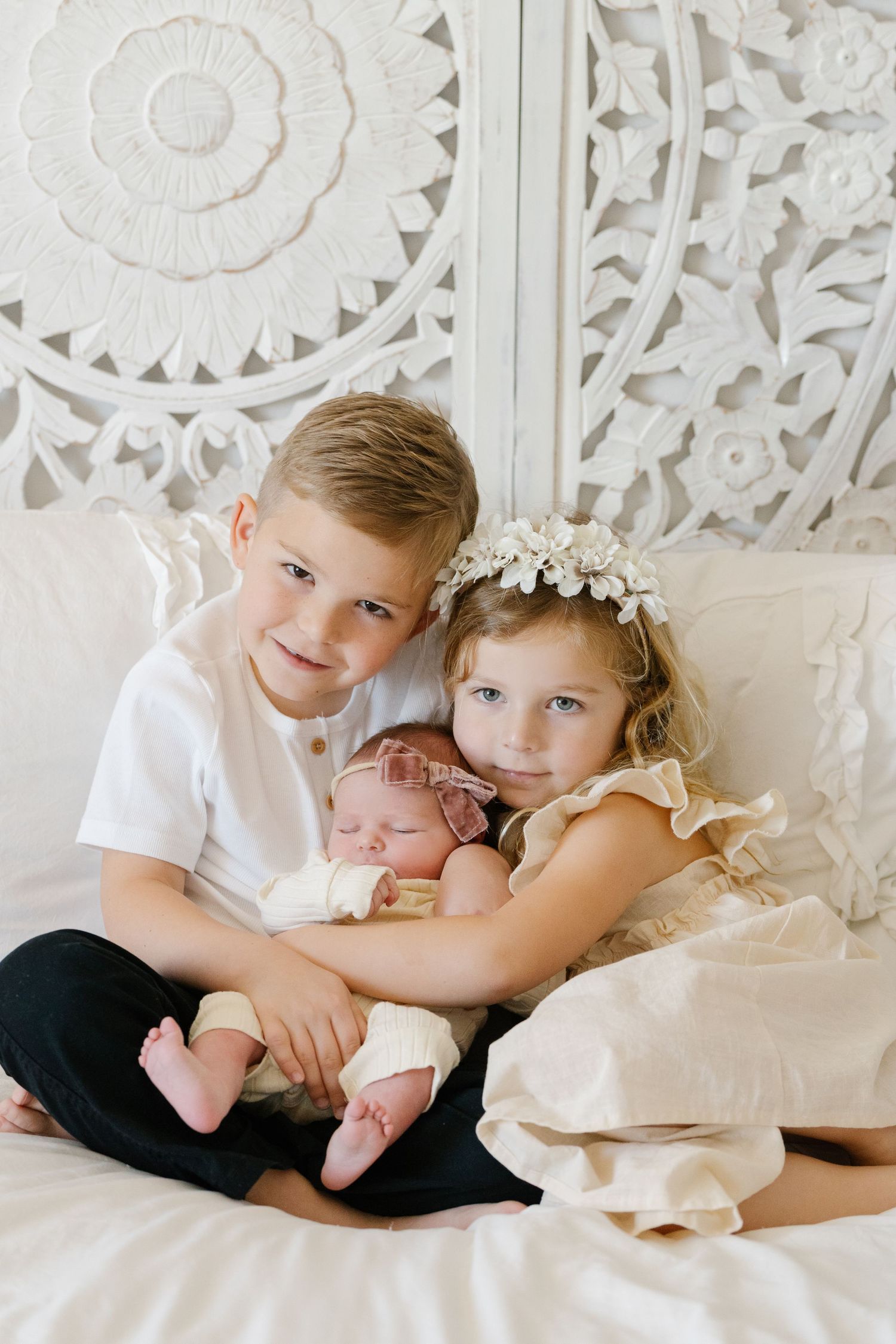 Three siblings pose together against an ornate white wall background.