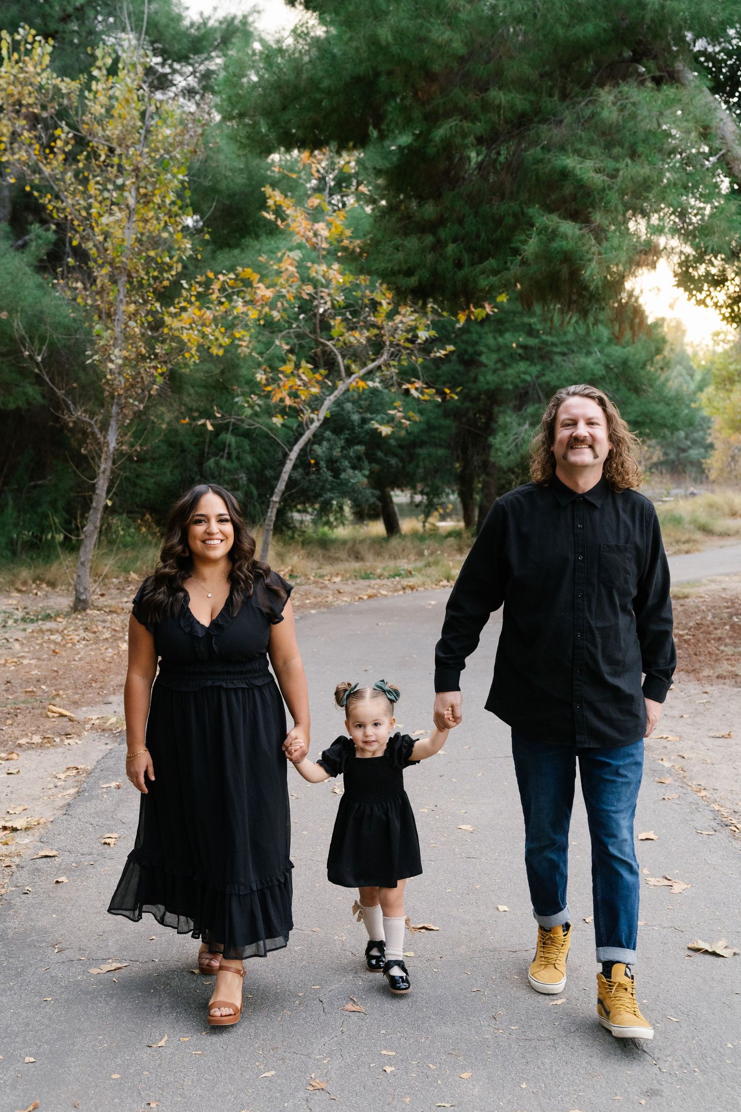 Family takes a stroll together on a path through autumn trees wearing coordinated black outfits.