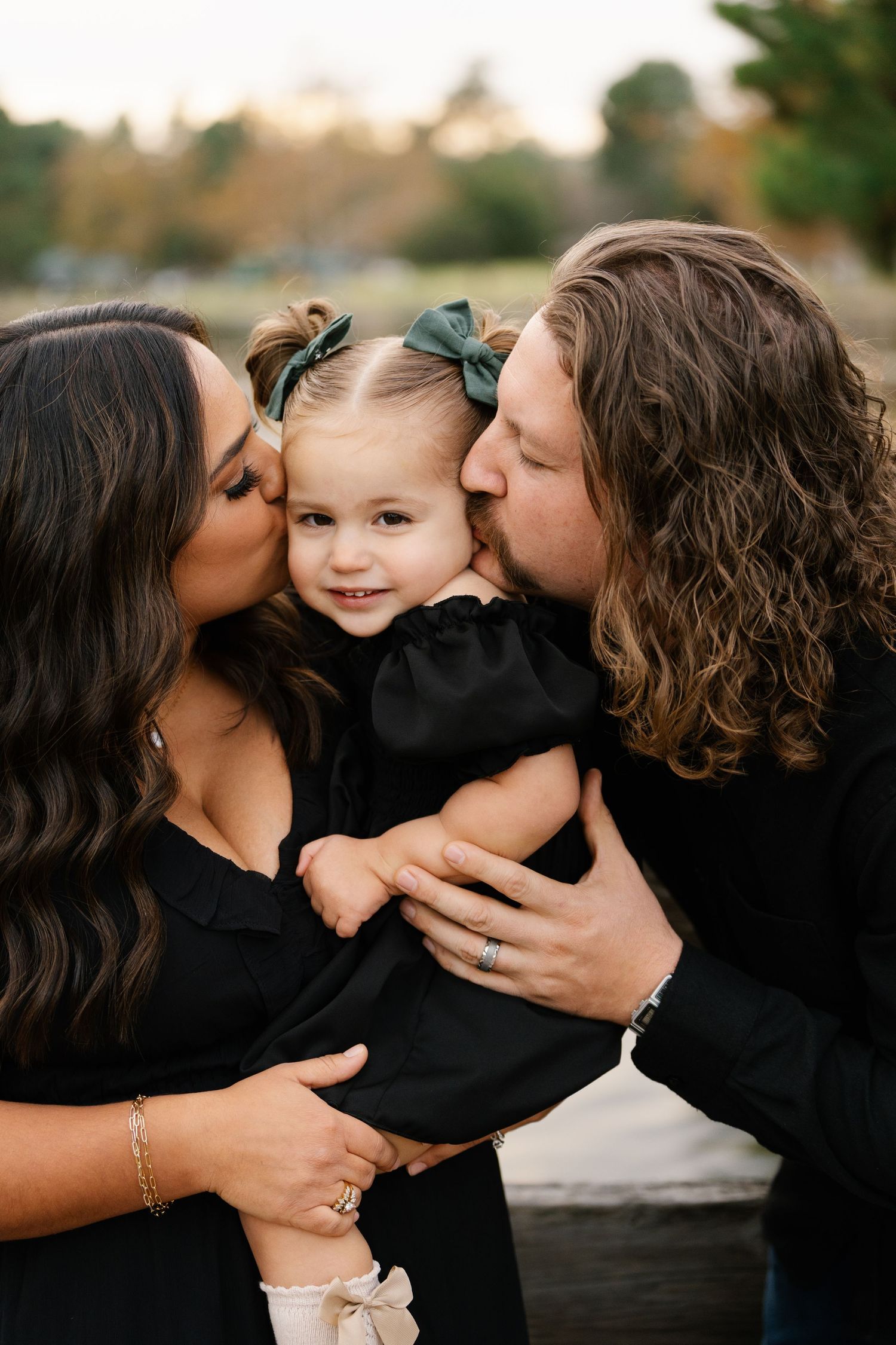Tender family moment captured in matching black outfits against a natural outdoor setting.