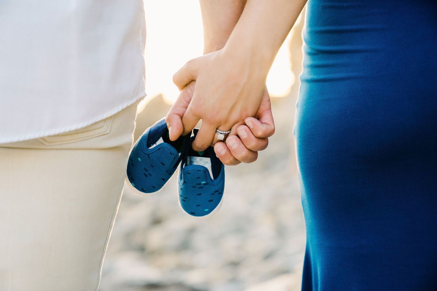 Close-up of hands holding tiny blue baby shoes against blurred background.