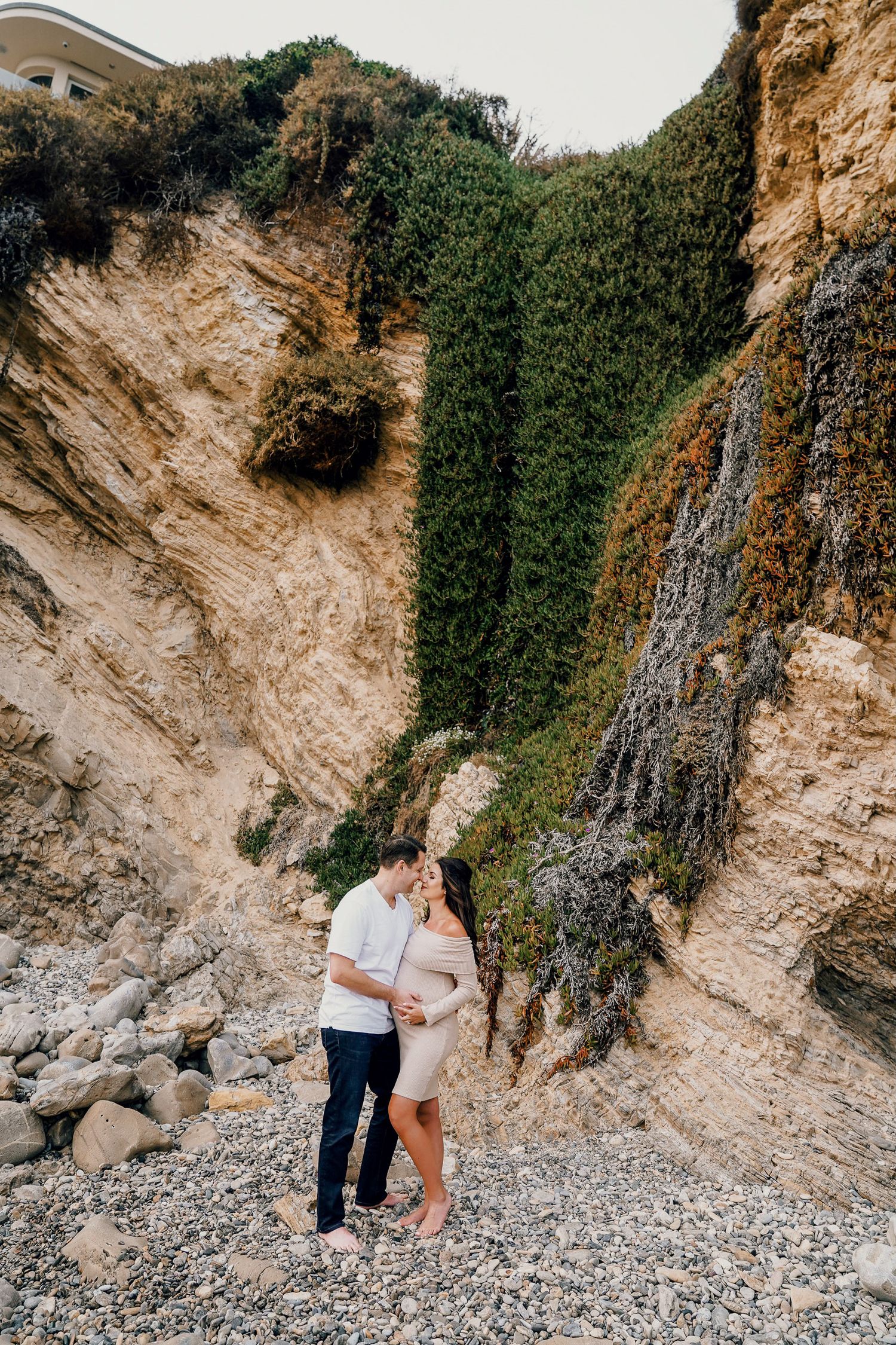 Couple shares intimate moment against dramatic coastal cliff backdrop.