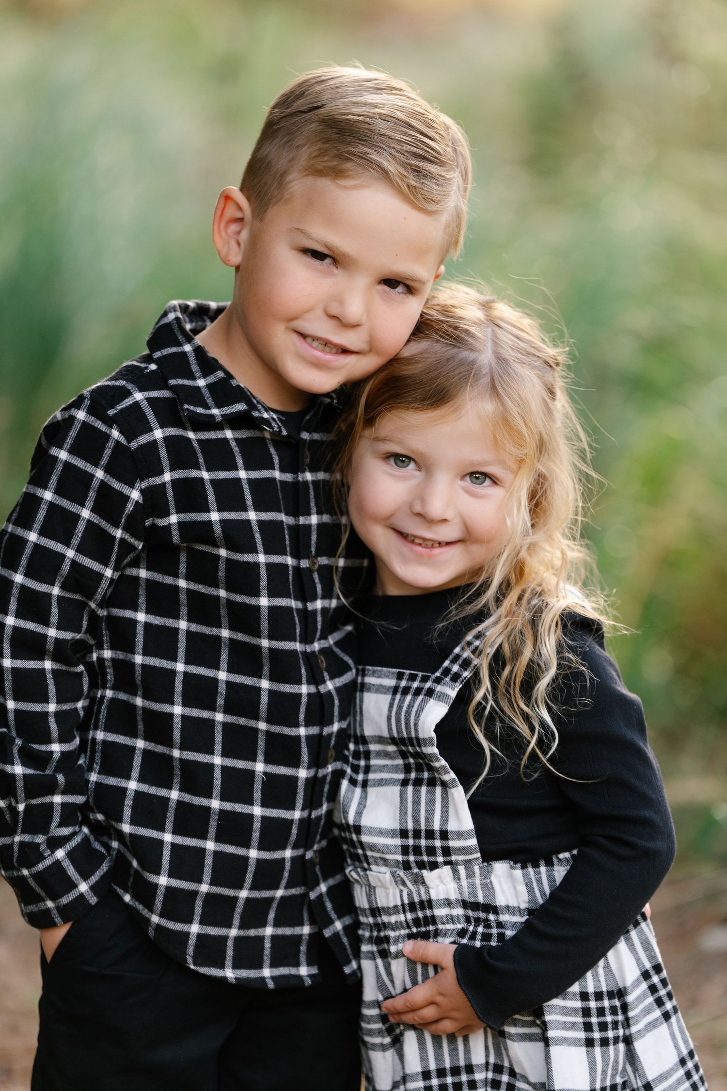 Two children in black and white plaid outfits pose together outdoors.