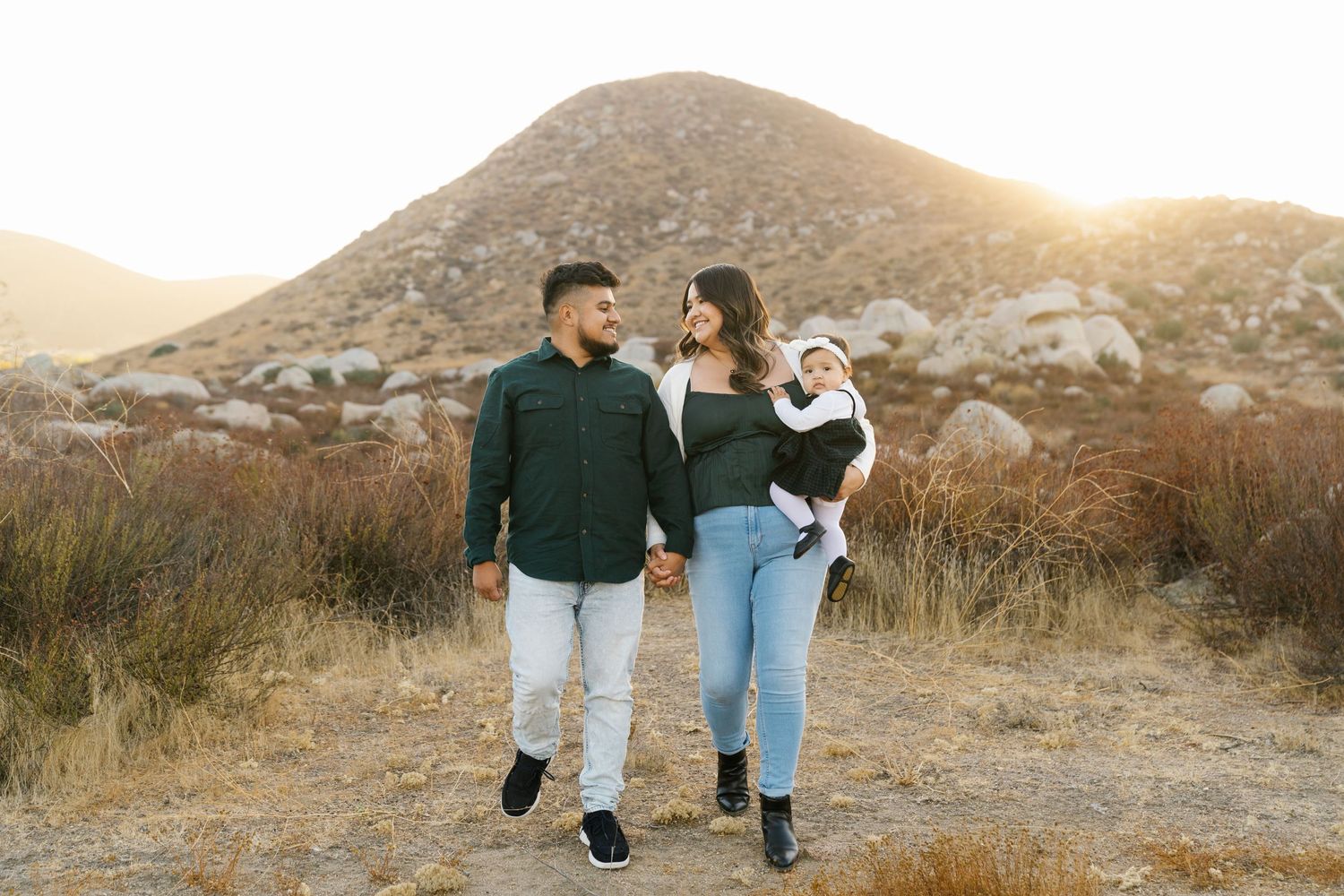 Family walking together on desert trail with mountains in background at sunset.