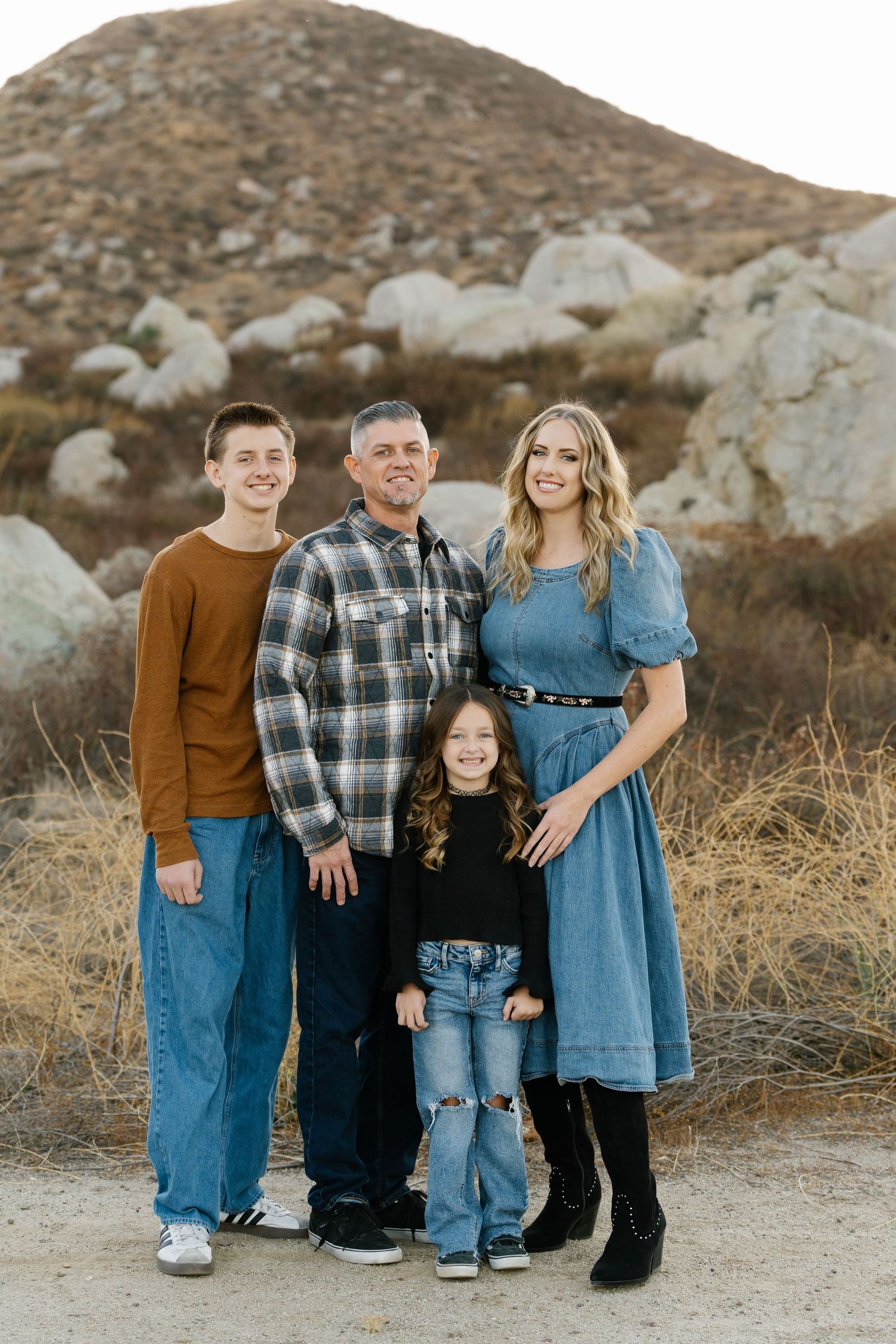A family of four poses together outdoors with rocky terrain and mountains in the background.