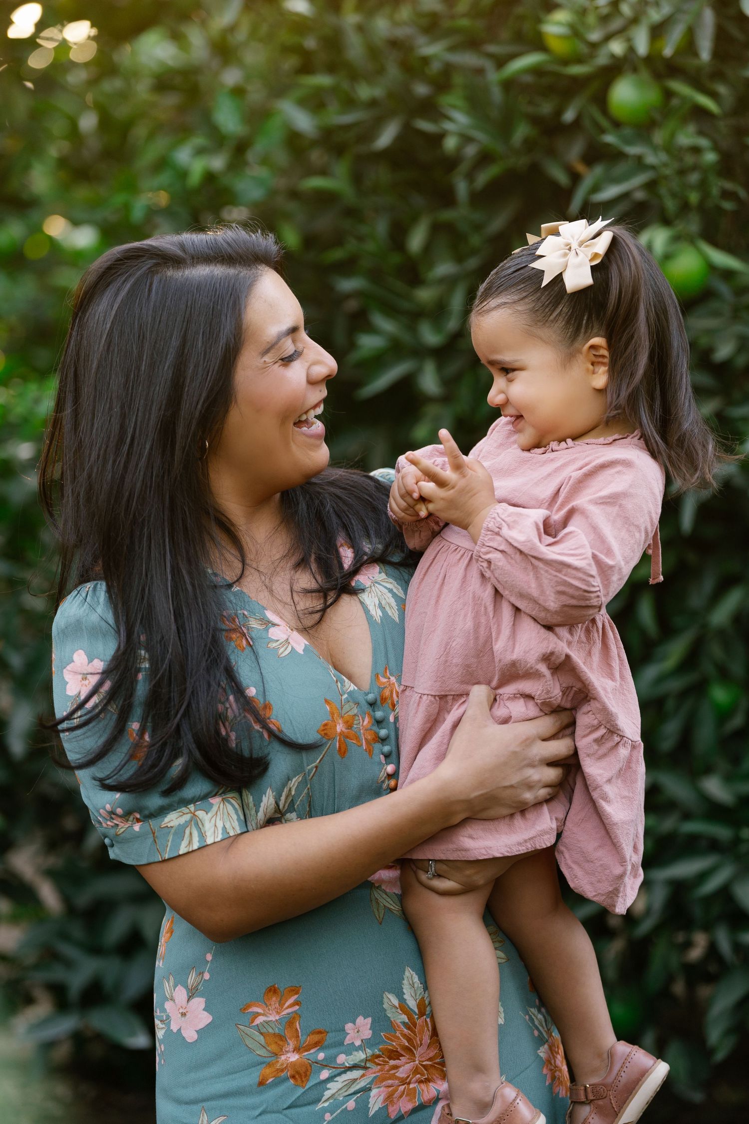 A tender moment between parent and child in matching pink and floral outfits against a lush garden backdrop.