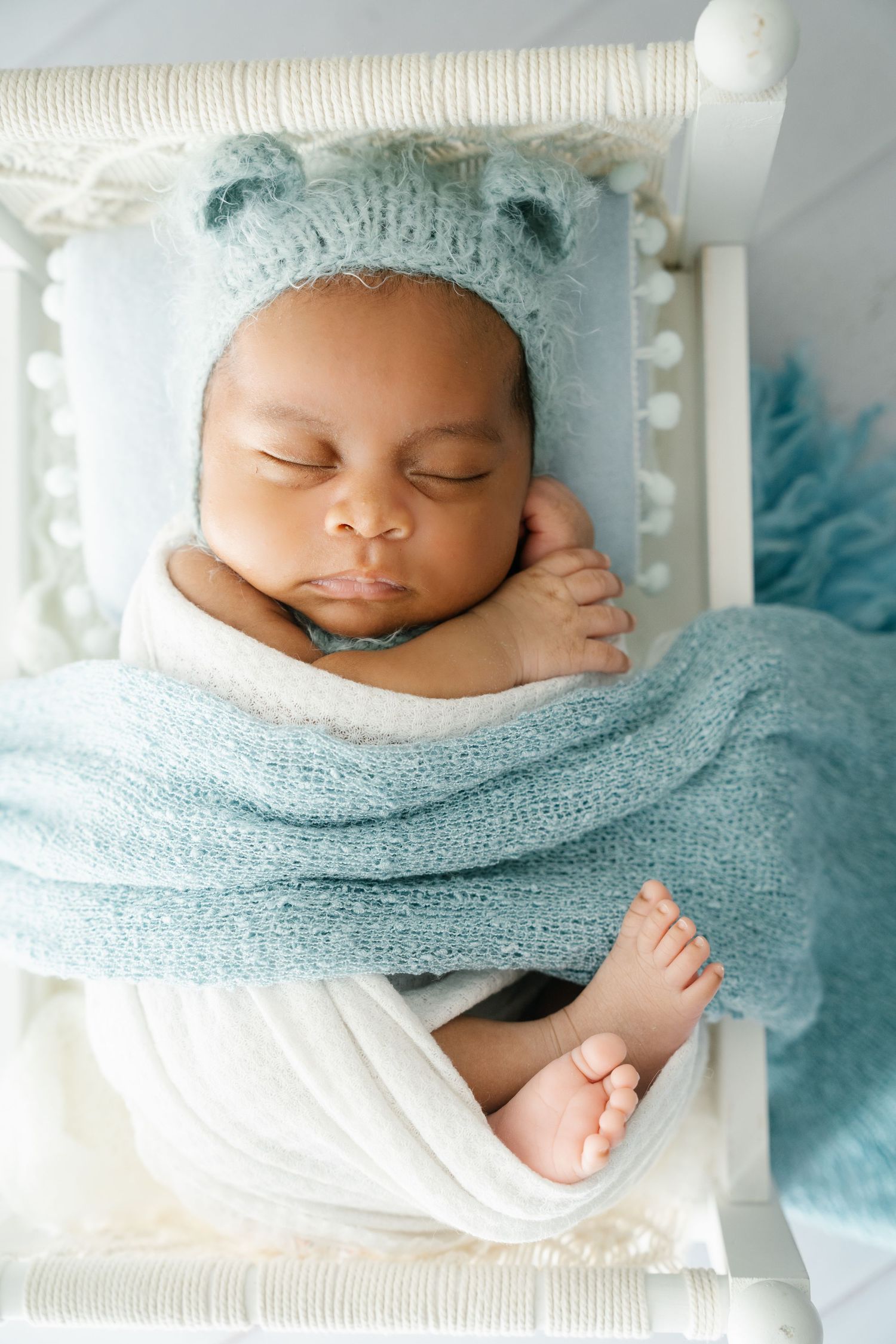 A peaceful sleeping baby wearing a blue knit hat nestled in soft white and blue blankets.