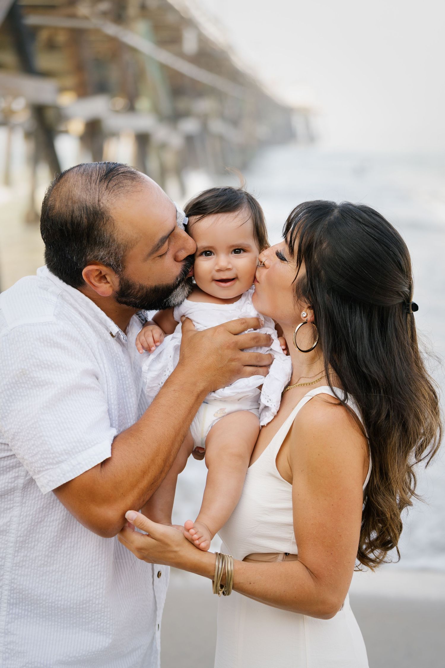 Loving family moment captured at beach with pier backdrop.