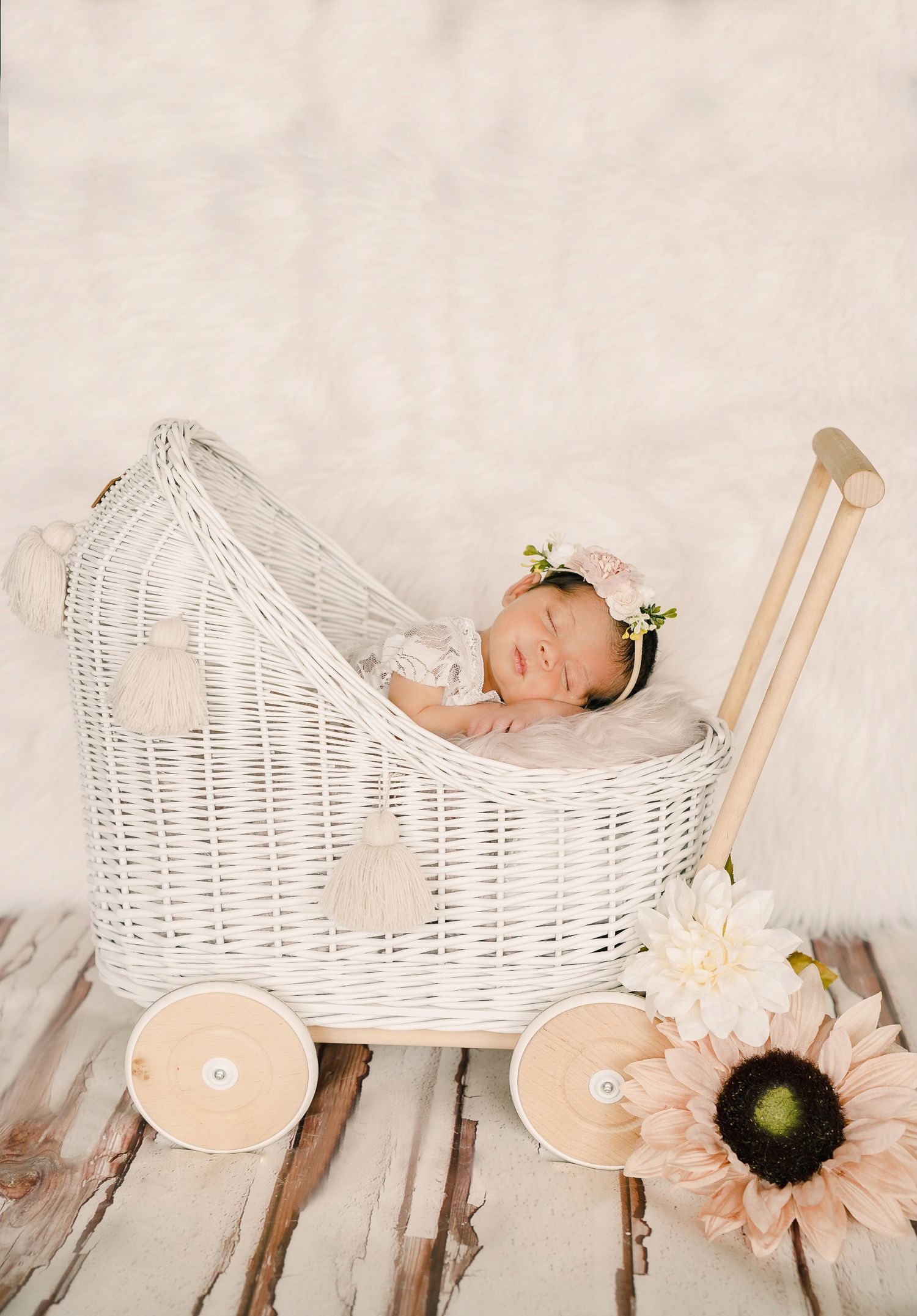 Sleeping newborn with floral crown in decorative white wicker carriage with sunflower decor.