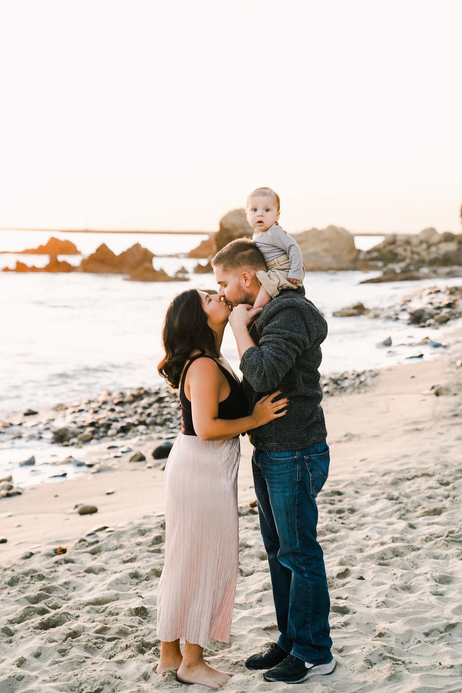 Family sharing intimate moment on rocky beach at sunset.
