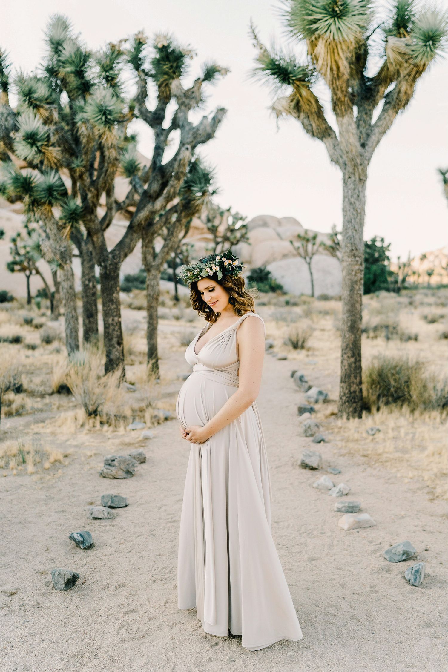 Maternity photo in desert featuring expecting mother in flowing dress surrounded by Joshua trees.
