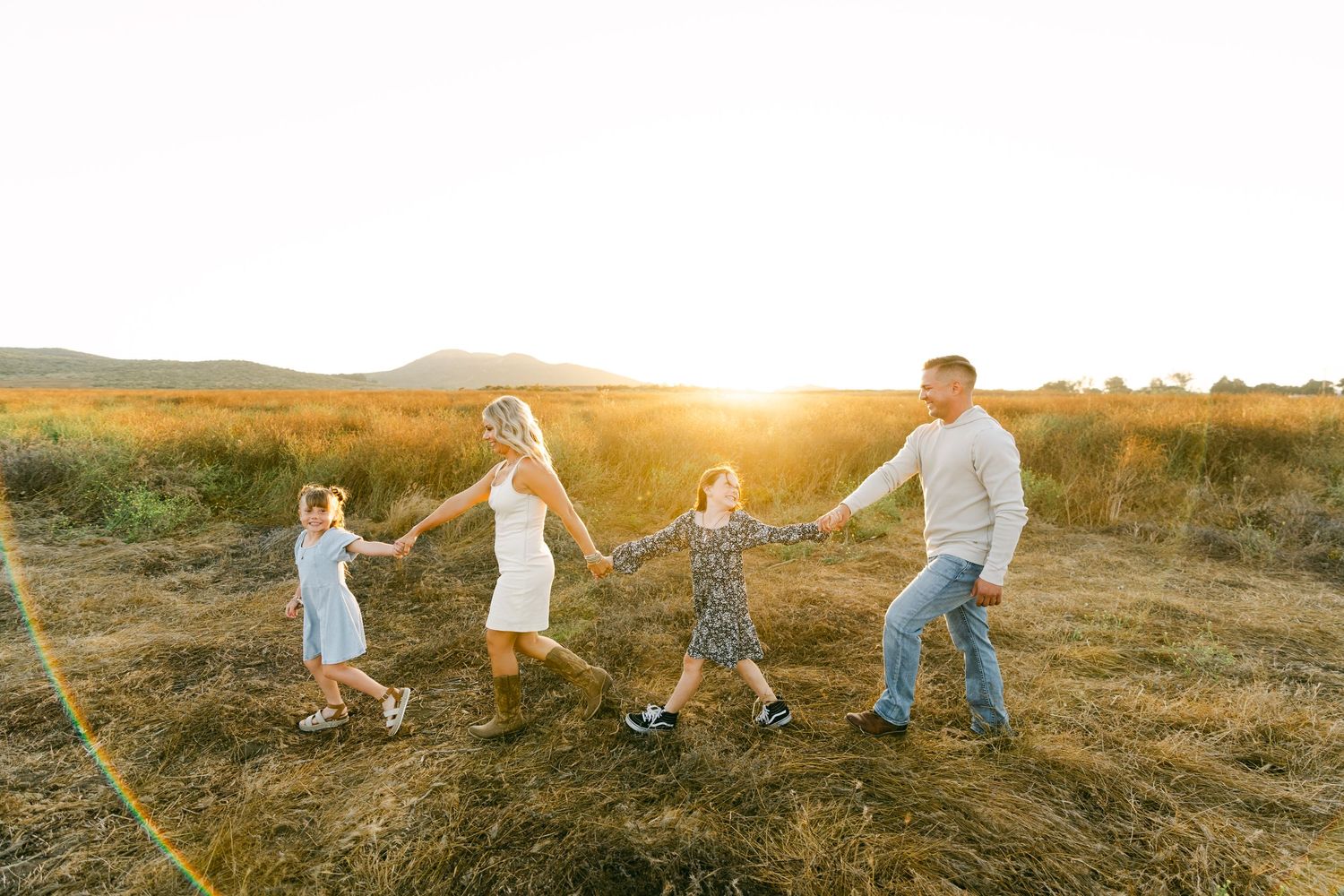 Family holding hands and dancing together in a field at golden hour.