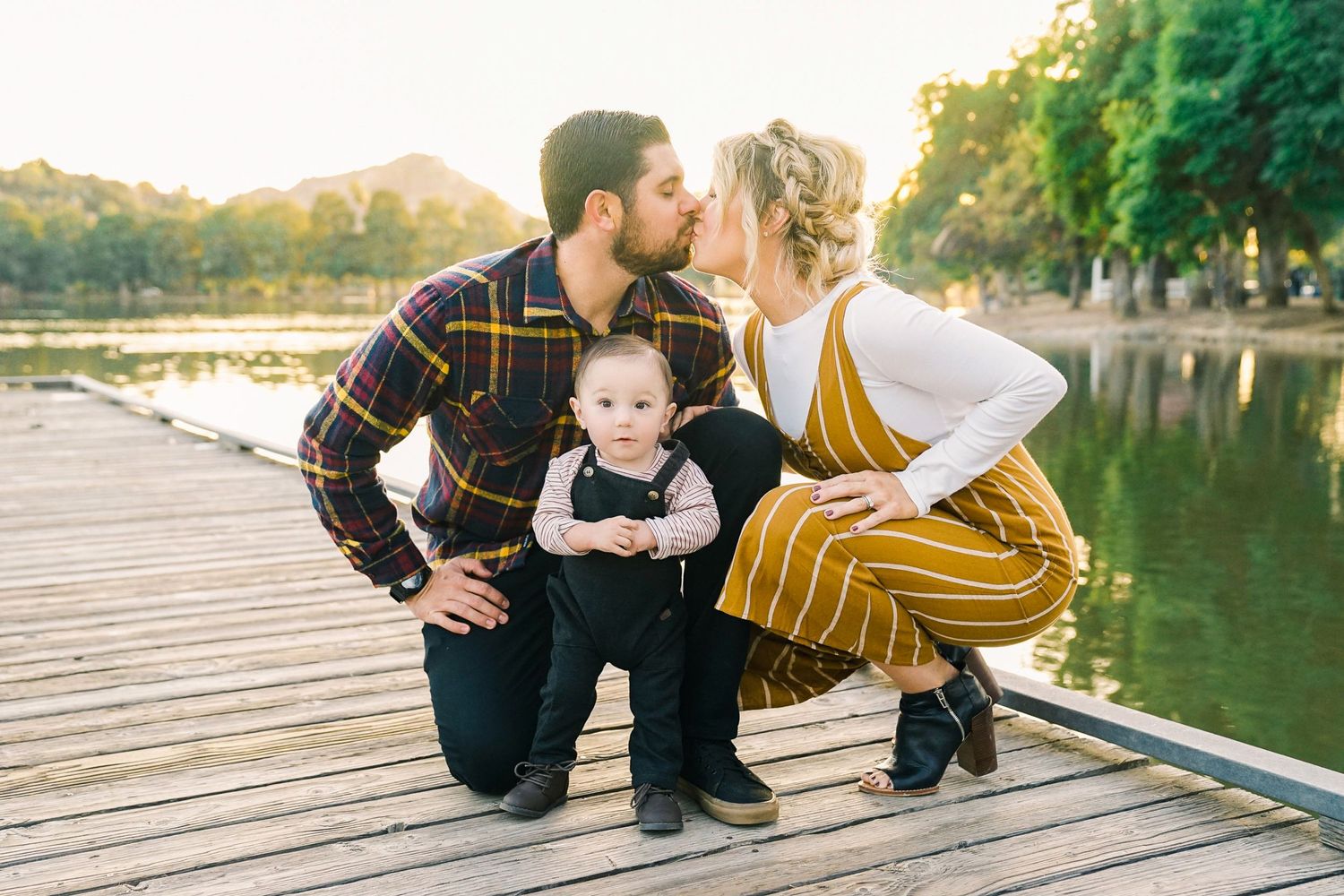 Family sharing tender moment together on wooden dock by lake at sunset.