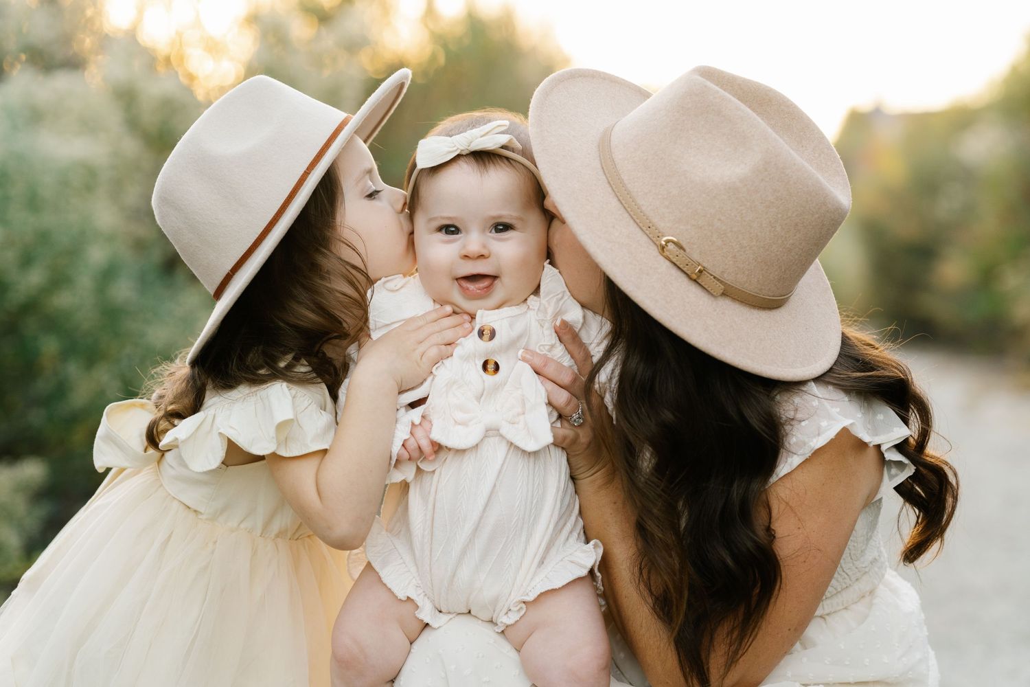 Two people in hats share sweet moment with baby wearing white ruffled outfit.