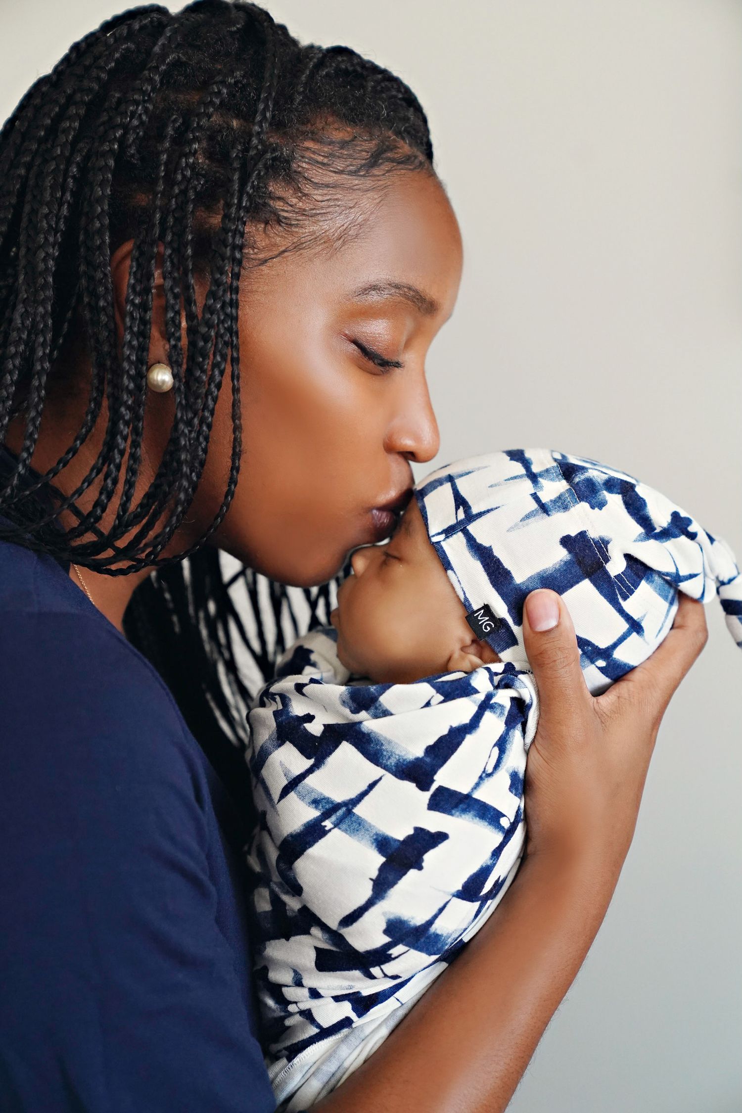Mother in navy shirt kissing newborn wrapped in blue and white patterned swaddle.