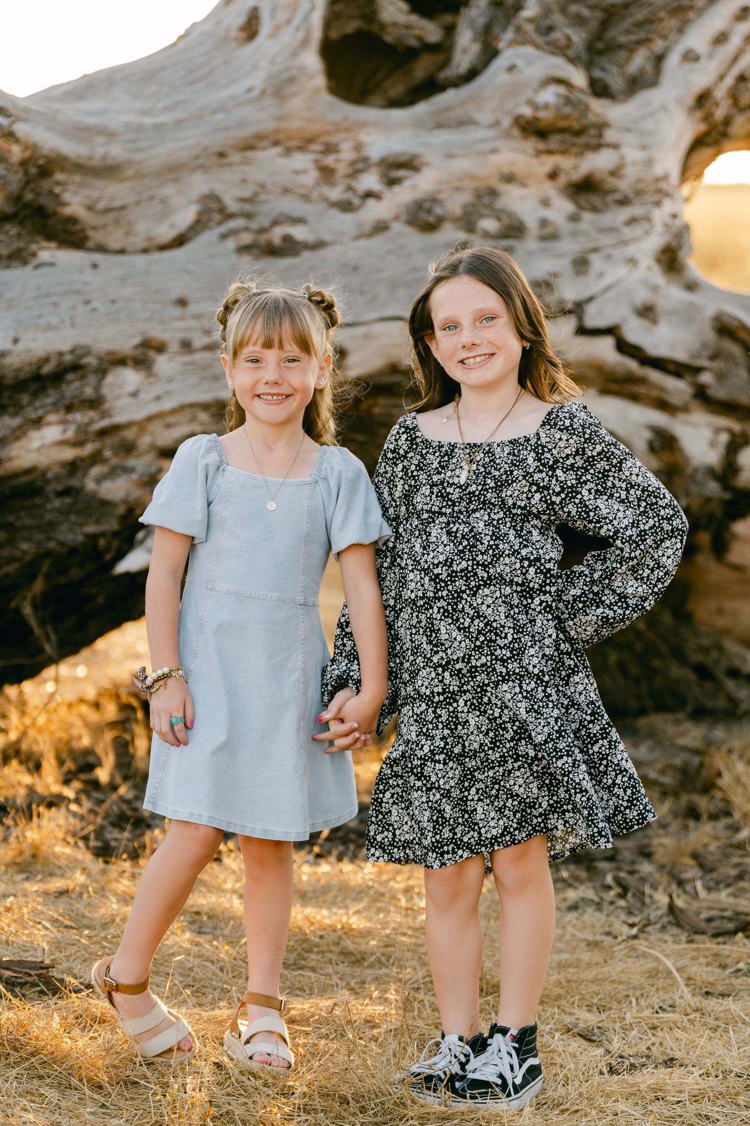 Two young friends in casual dresses pose together against rocky natural backdrop.