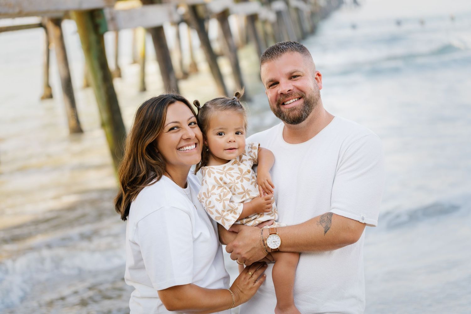 Happy family portrait at beach pier wearing coordinated white outfits.