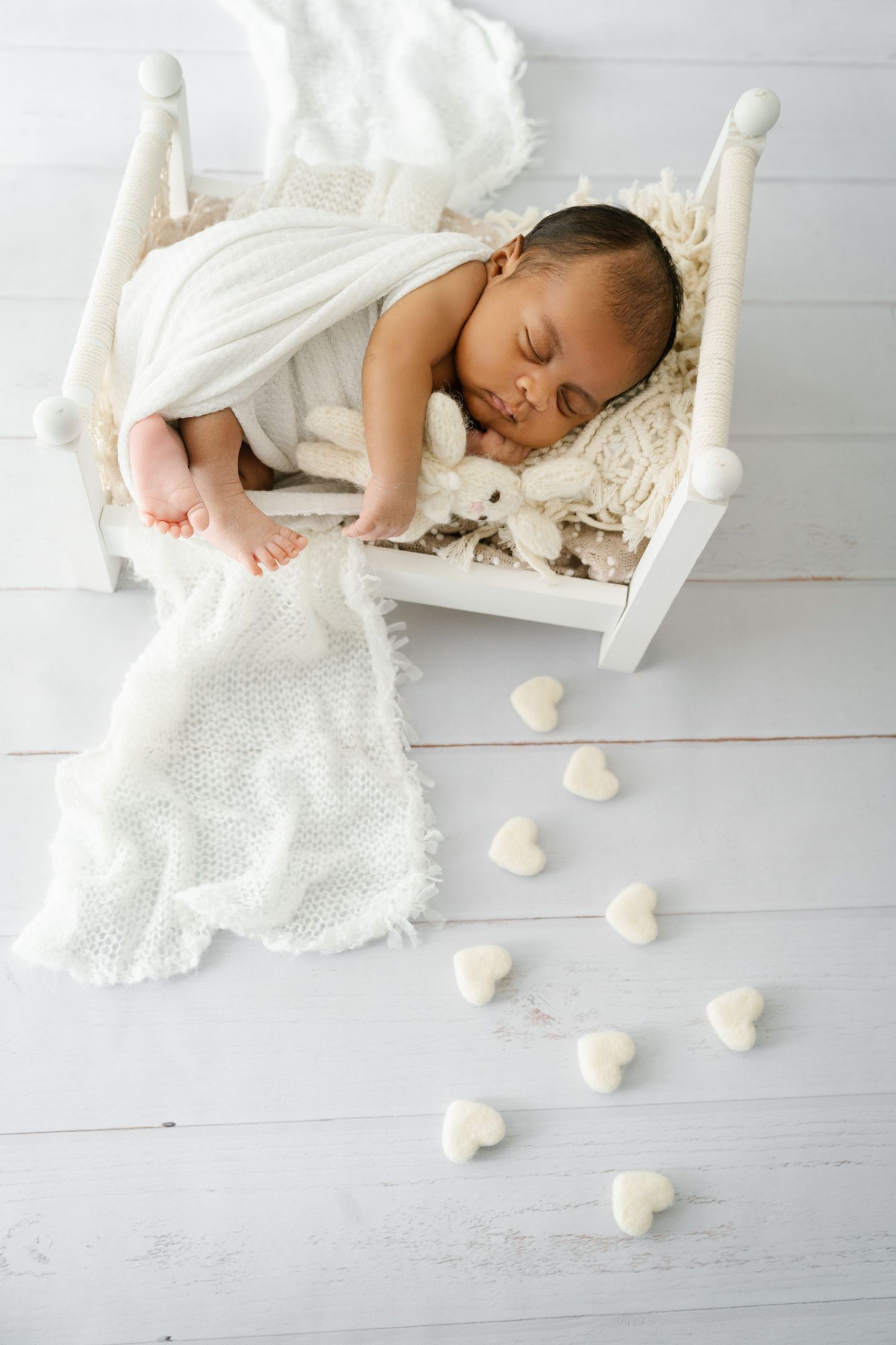 Sleeping baby in white wooden cradle with scattered heart decorations on gray floor.