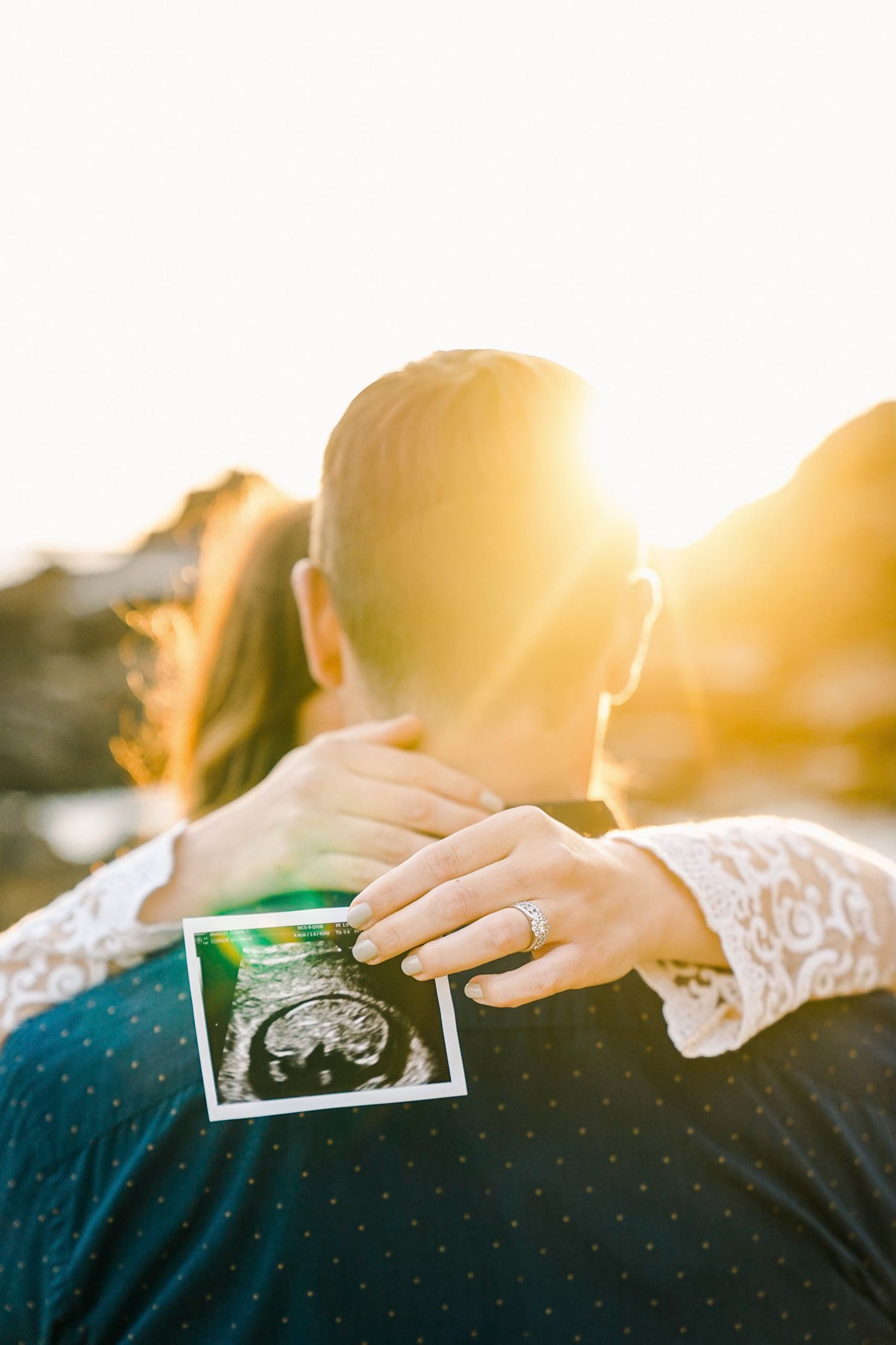 Close-up of hands holding ultrasound photo during sunset maternity session.