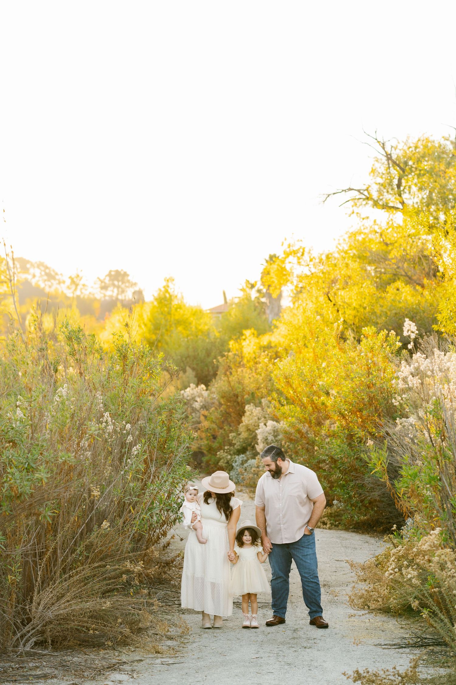 Family walking together on a path surrounded by vibrant yellow wildflowers during golden hour.