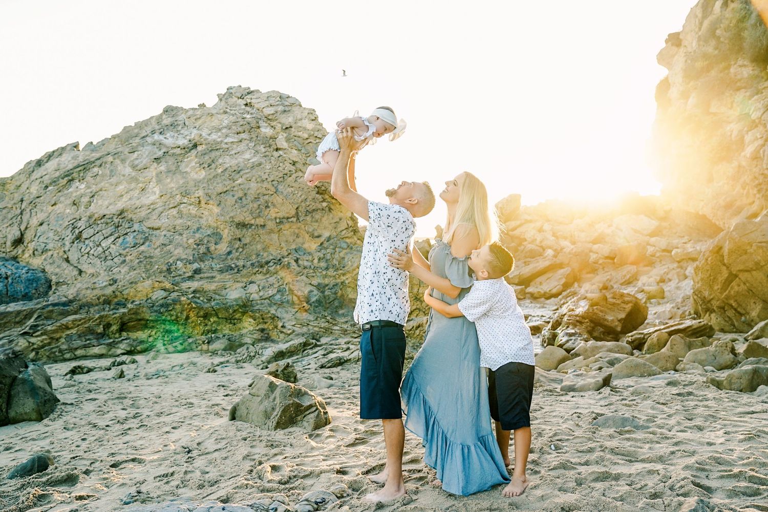 A family sharing a playful moment on rocky beach terrain at sunset.