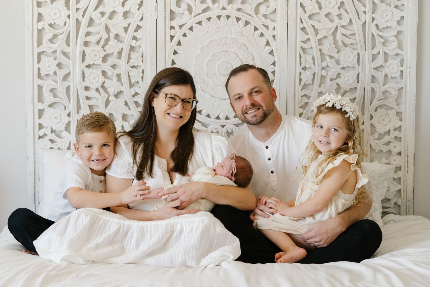 Family portrait with parents and children sitting against ornate white wall panel.