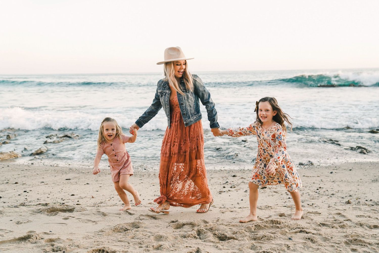 Parent and children holding hands while playing on beach at sunset.