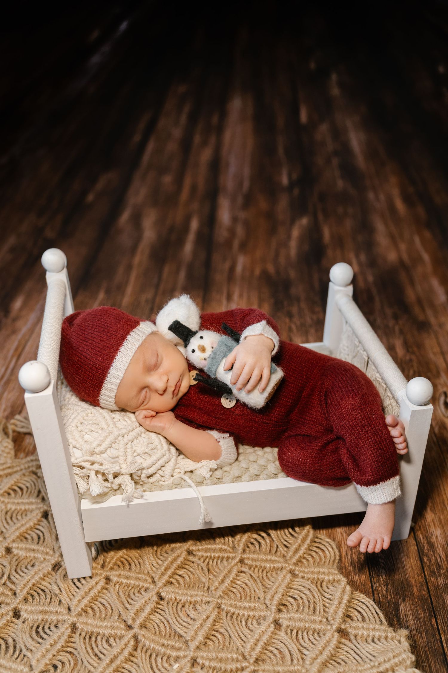 Sleeping infant in red outfit on small white bed with decorative wooden floor.