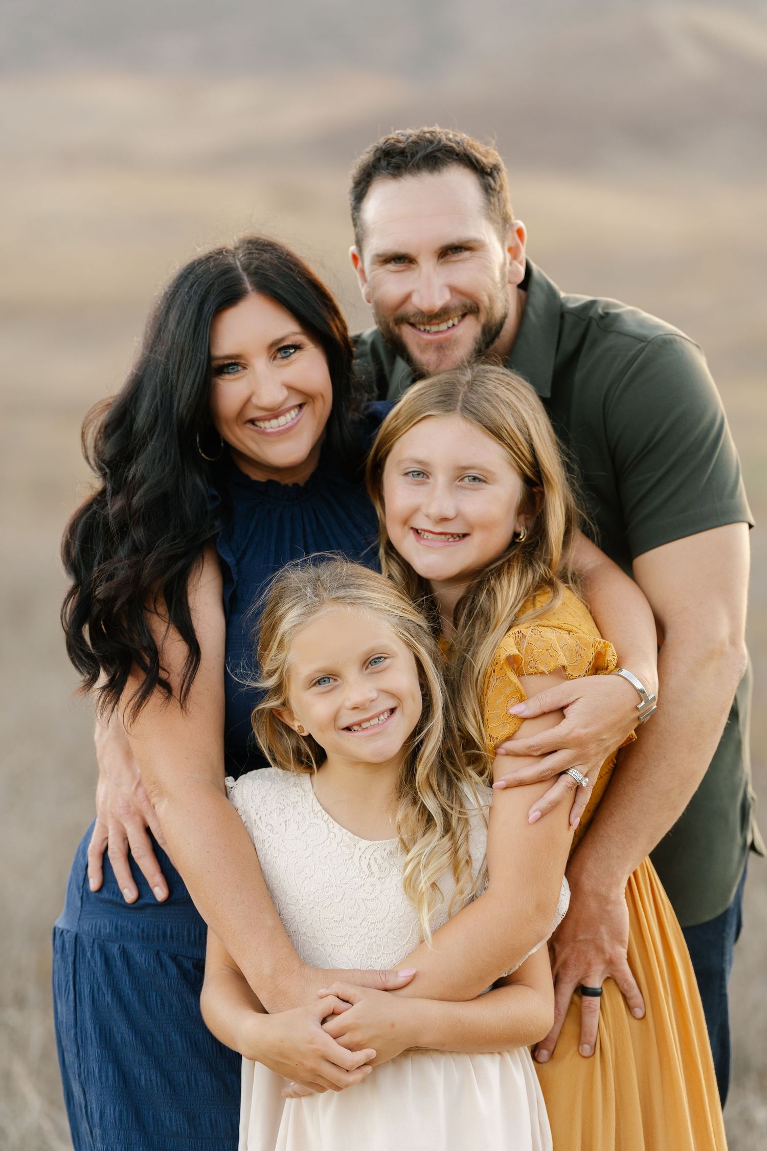 Smiling family of four embracing closely outdoors in warm golden light.