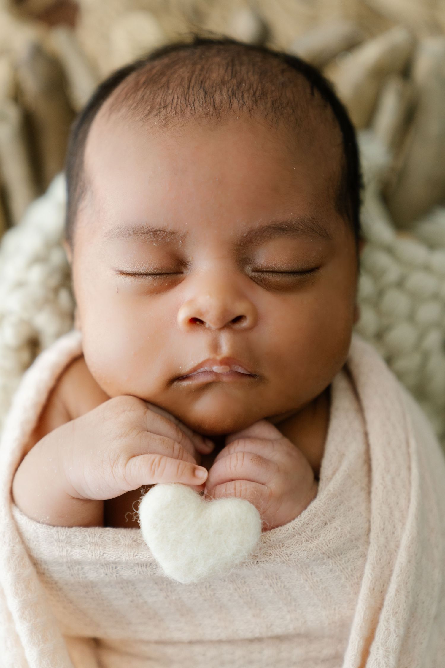 Sleeping infant wrapped in cream swaddle holding small white heart.