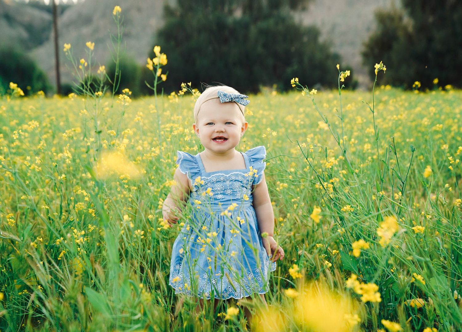 Child in blue floral dress surrounded by blooming yellow wildflowers.