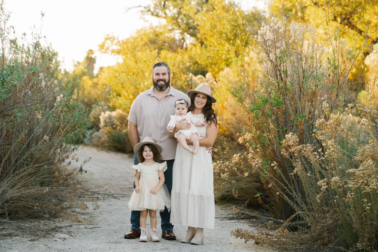 A family of four poses together on a desert path surrounded by golden autumn foliage.