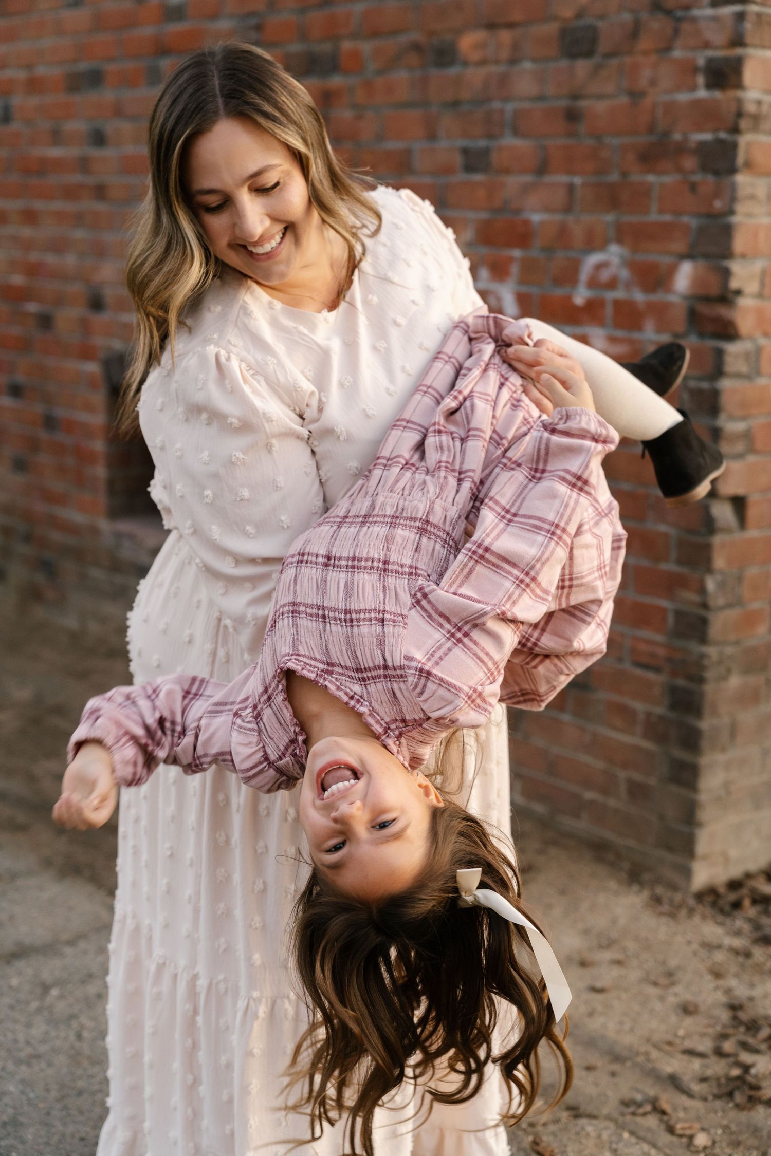 Playful upside-down moment captured against rustic brick wall background.