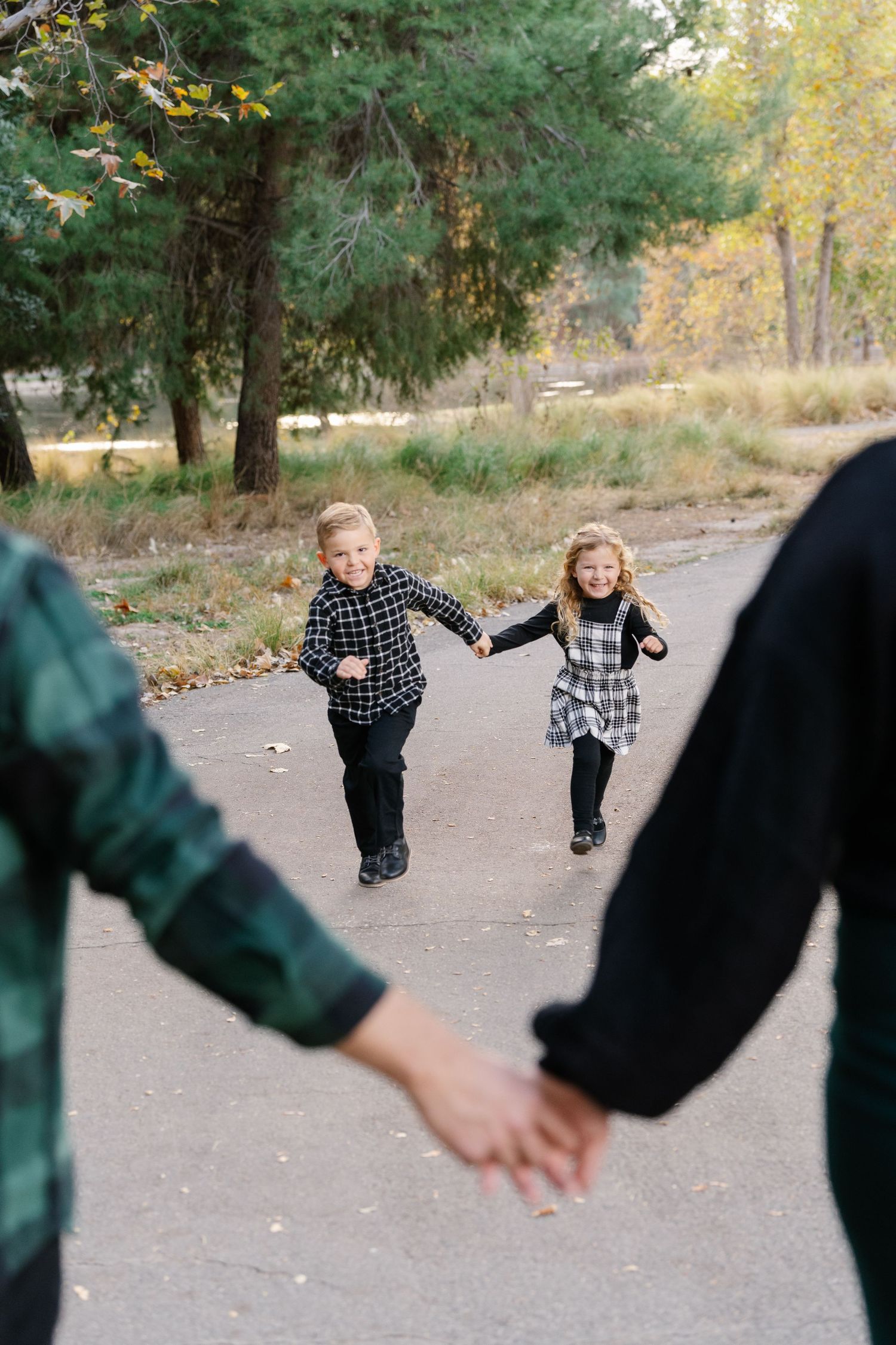 Two children run playfully on a path while adults hold hands in the foreground.
