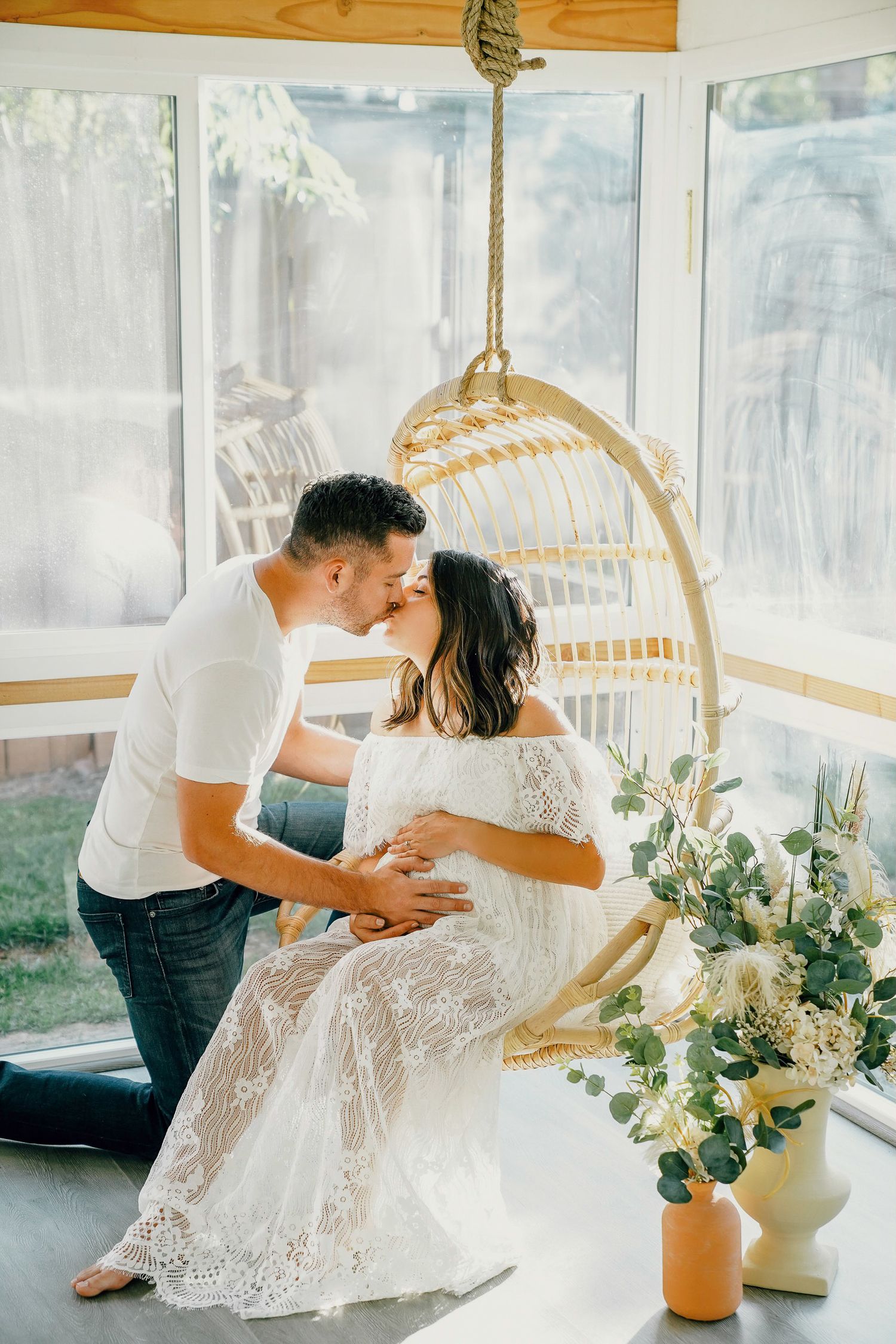 Intimate moment in a sunlit room with a hanging rattan chair and floral decorations.