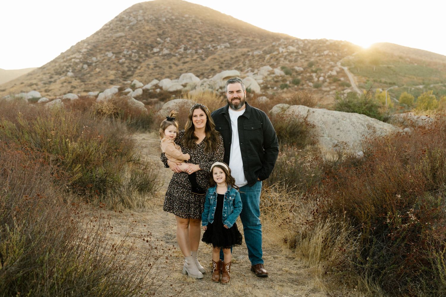 Family portrait in desert landscape with mountains and sunset in the background.
