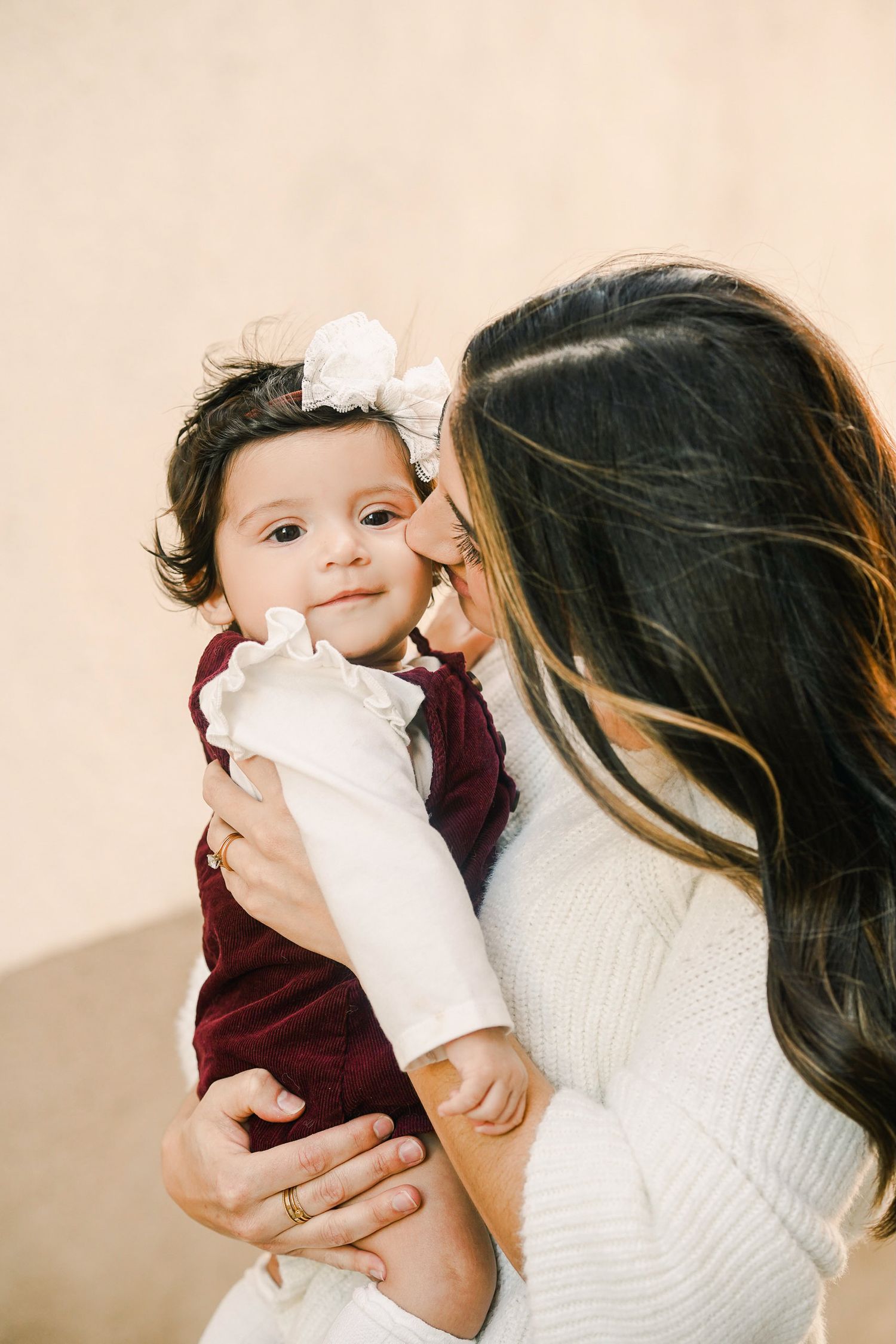 Tender moment between parent and baby in white and burgundy outfits.
