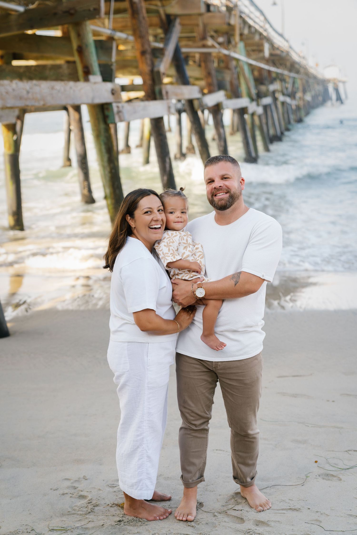 Beach family portrait with wooden pier in background.